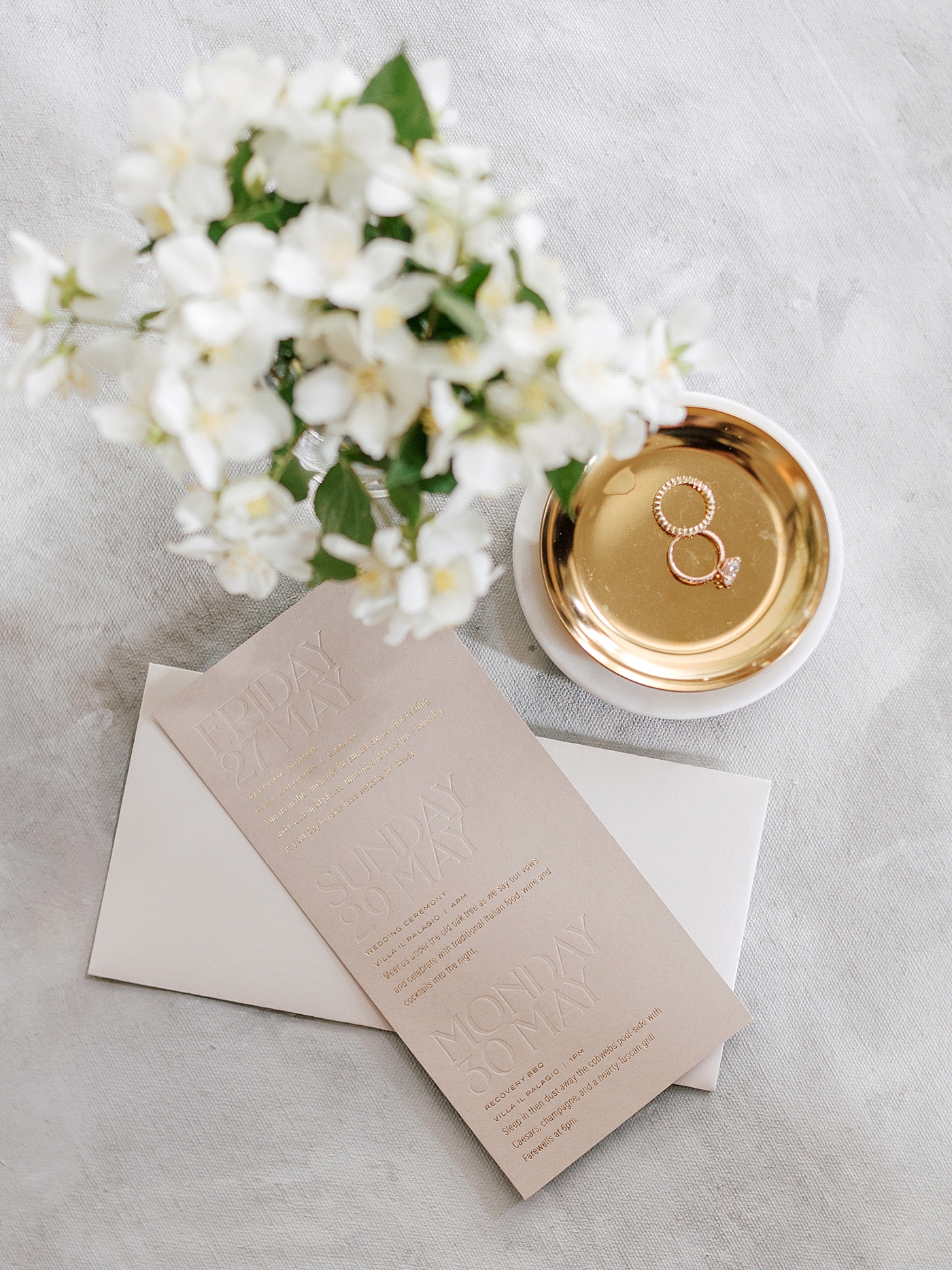 Gold ring dish with rings, white flowers, and a wedding invitation | Photo by NYC Wedding Photographer Hope Helmuth 