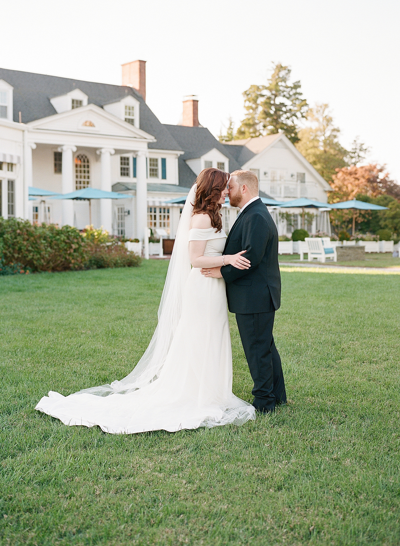 Bride and groom kissing on a lawn in front of a big white house | Photo by Hope Helmuth Photography