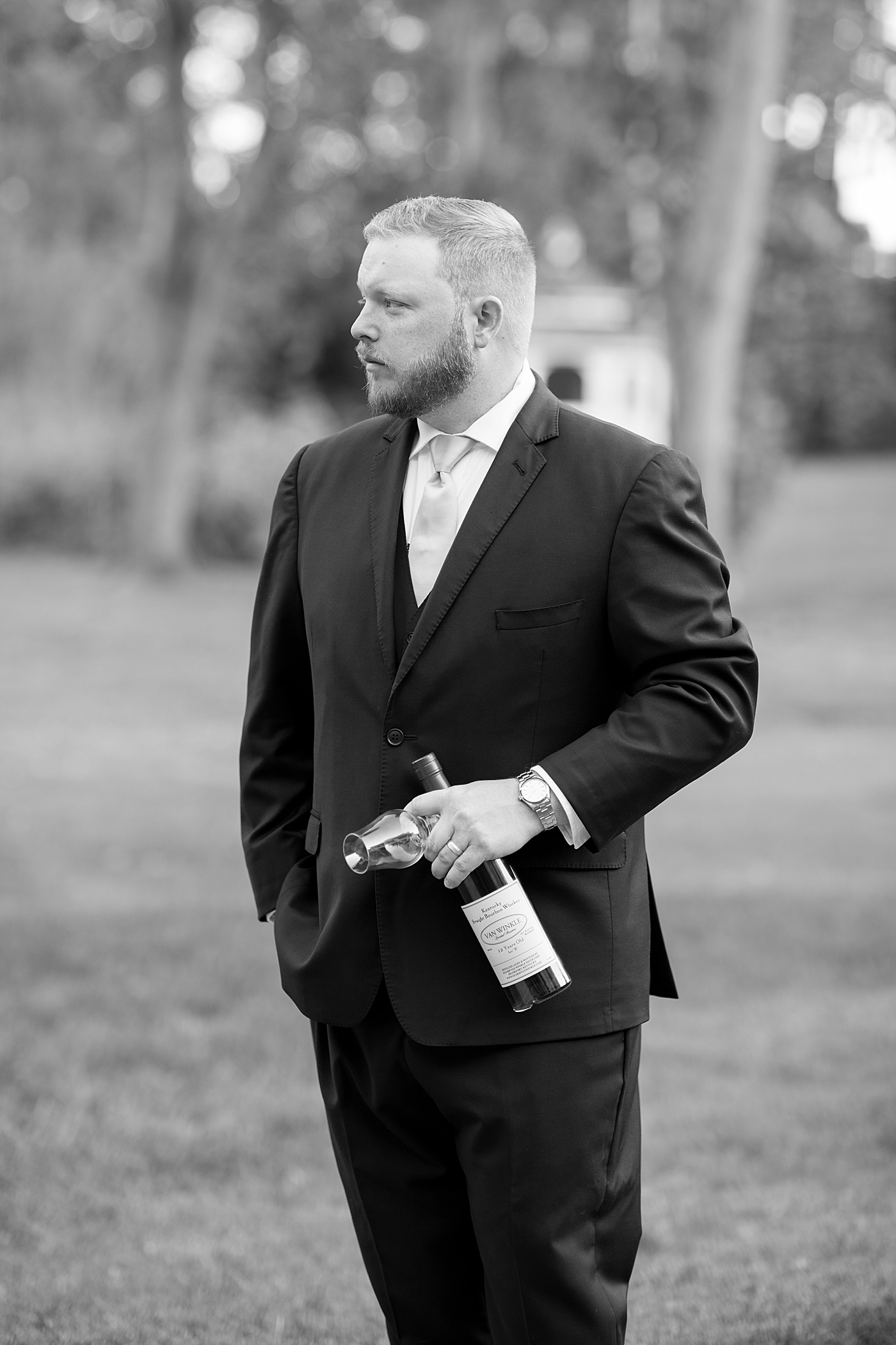 Black and white photo of groom holding bottle of bourbon | Photo by Hope Helmuth Photography
