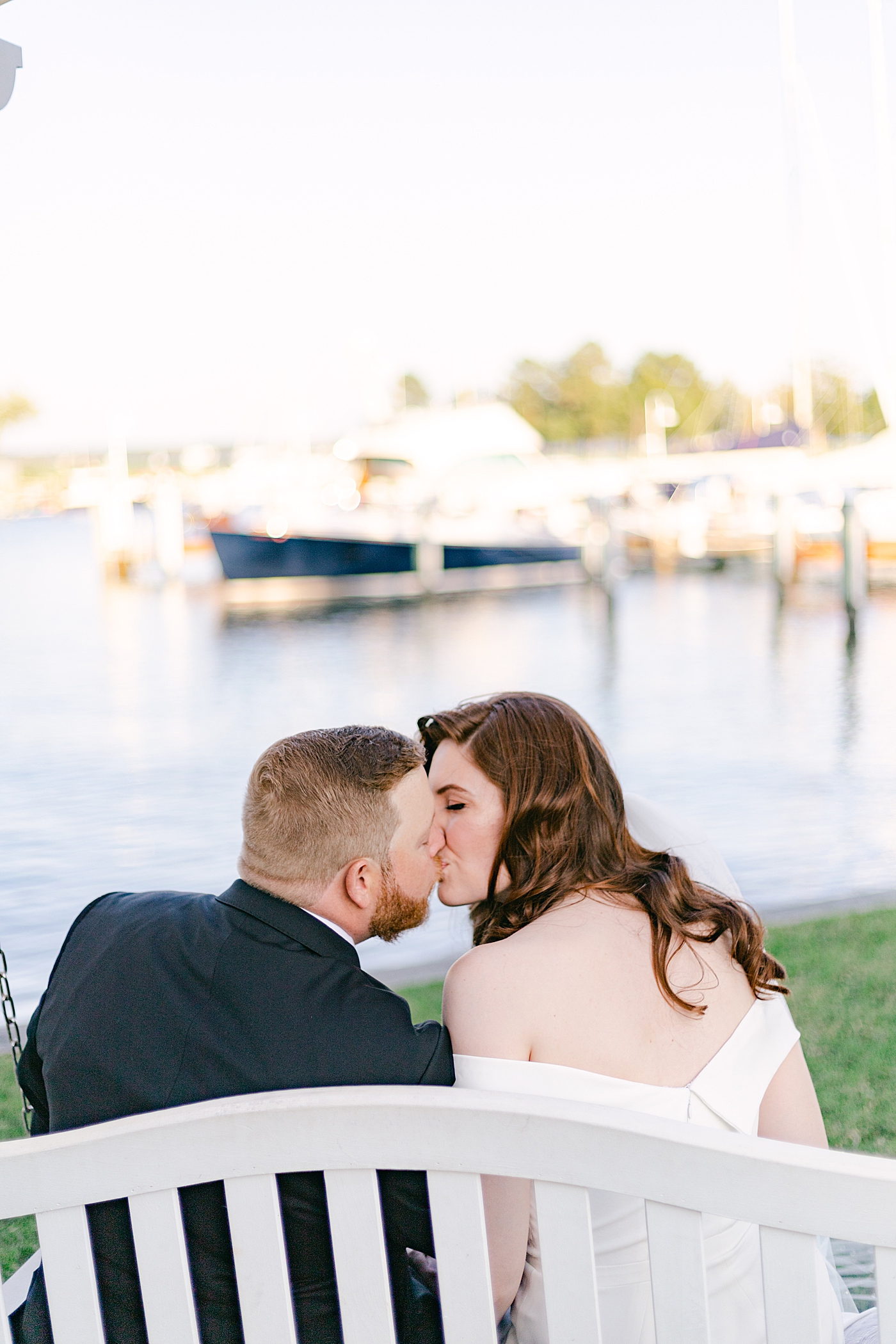 Bride and groom kiss on a bench near a harbor | Photo by Hope Helmuth Photography