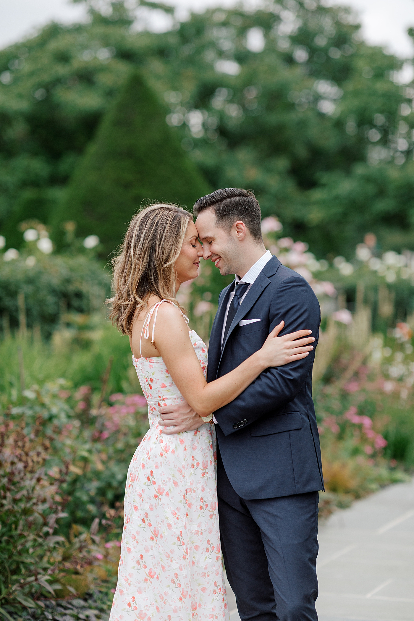 Couple embracing in a park with flowers blooming behind them | Engagement Session Guides by Hope Helmuth Photography