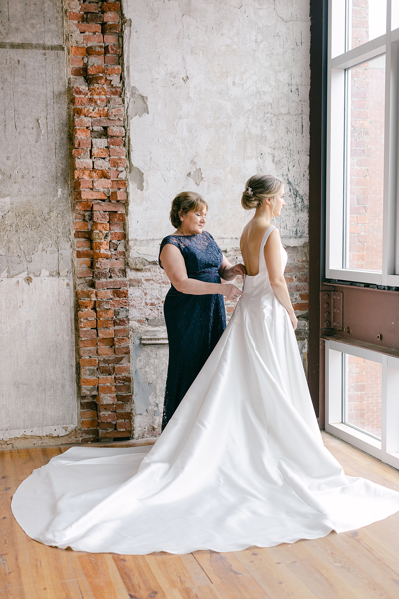 Mother of the bride helping the bride zip her dress | Photo by Hope Helmuth Photography