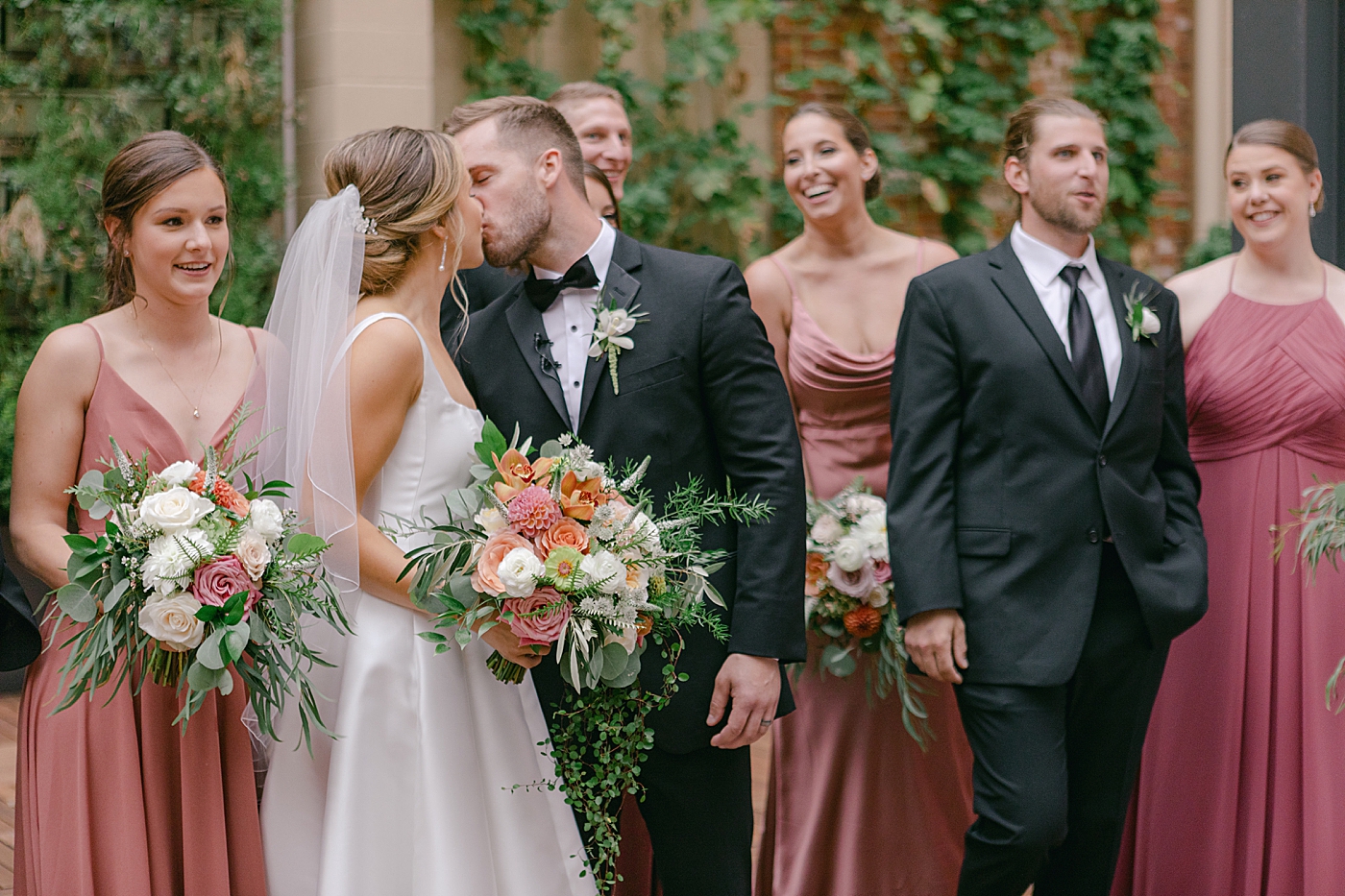 Bride and groom kissing with their wedding party in the background | Photo by Hope Helmuth Photography