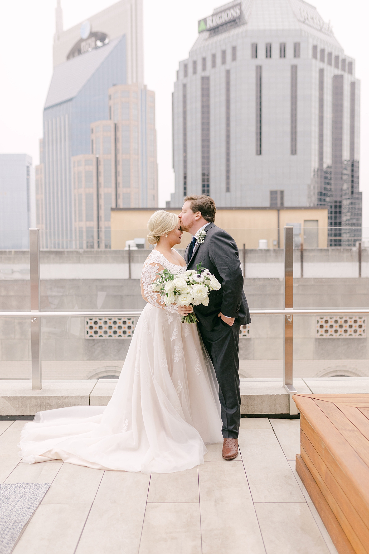Groom kissing bride on forehead on a rooftop in Nashville | Photo by Hope Helmuth Photography