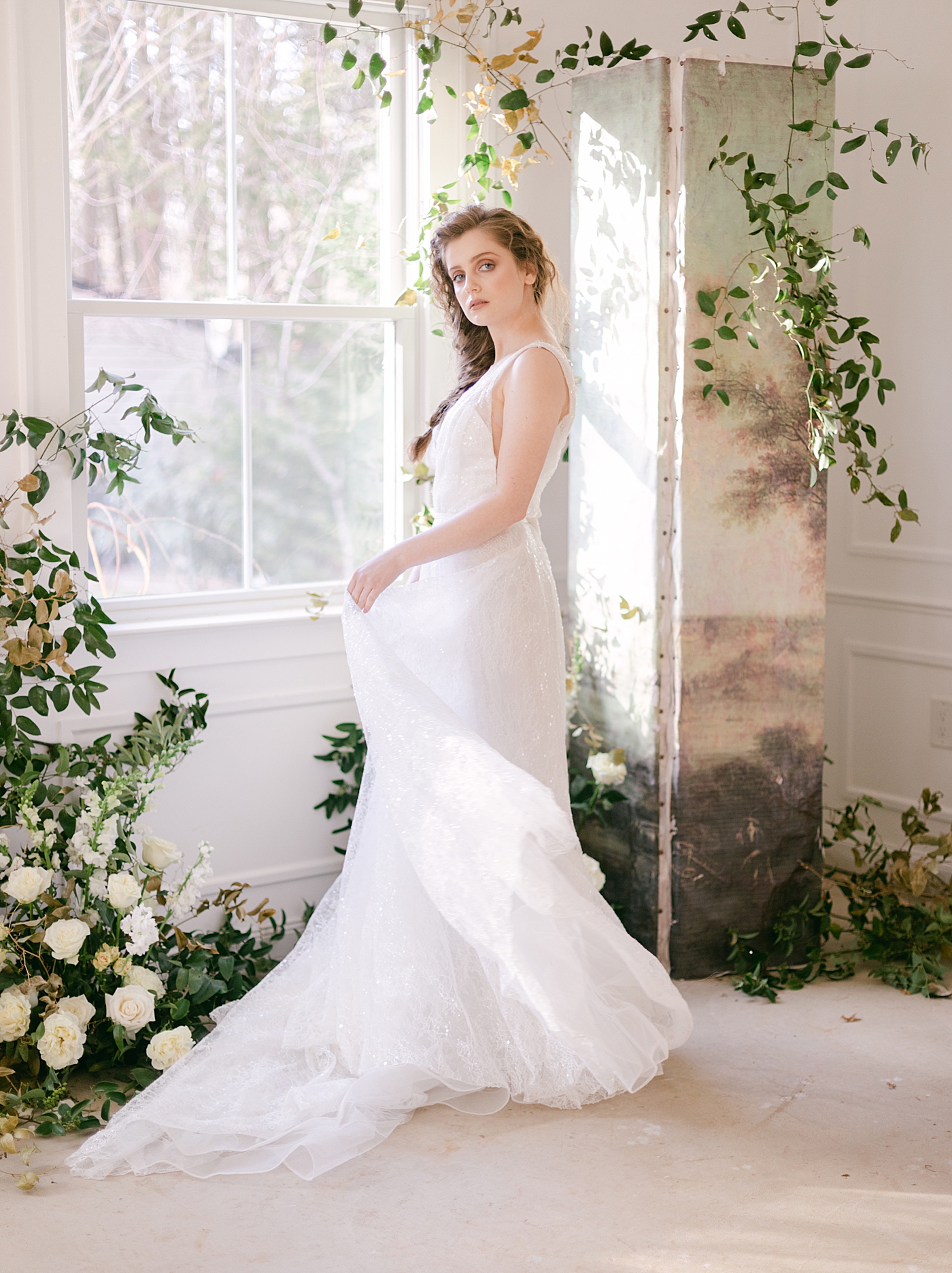 Bride near a window holding her dress | Photo by Hope Helmuth Photograpghy
