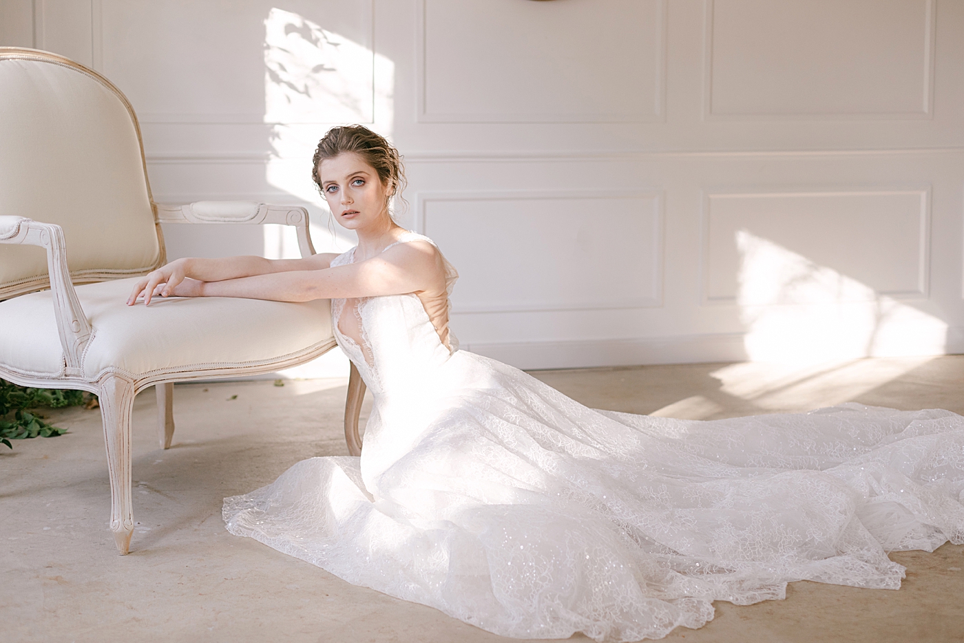 Bride in a gown sitting on a floor near a chair | Photo by Hope Helmuth Photograpghy