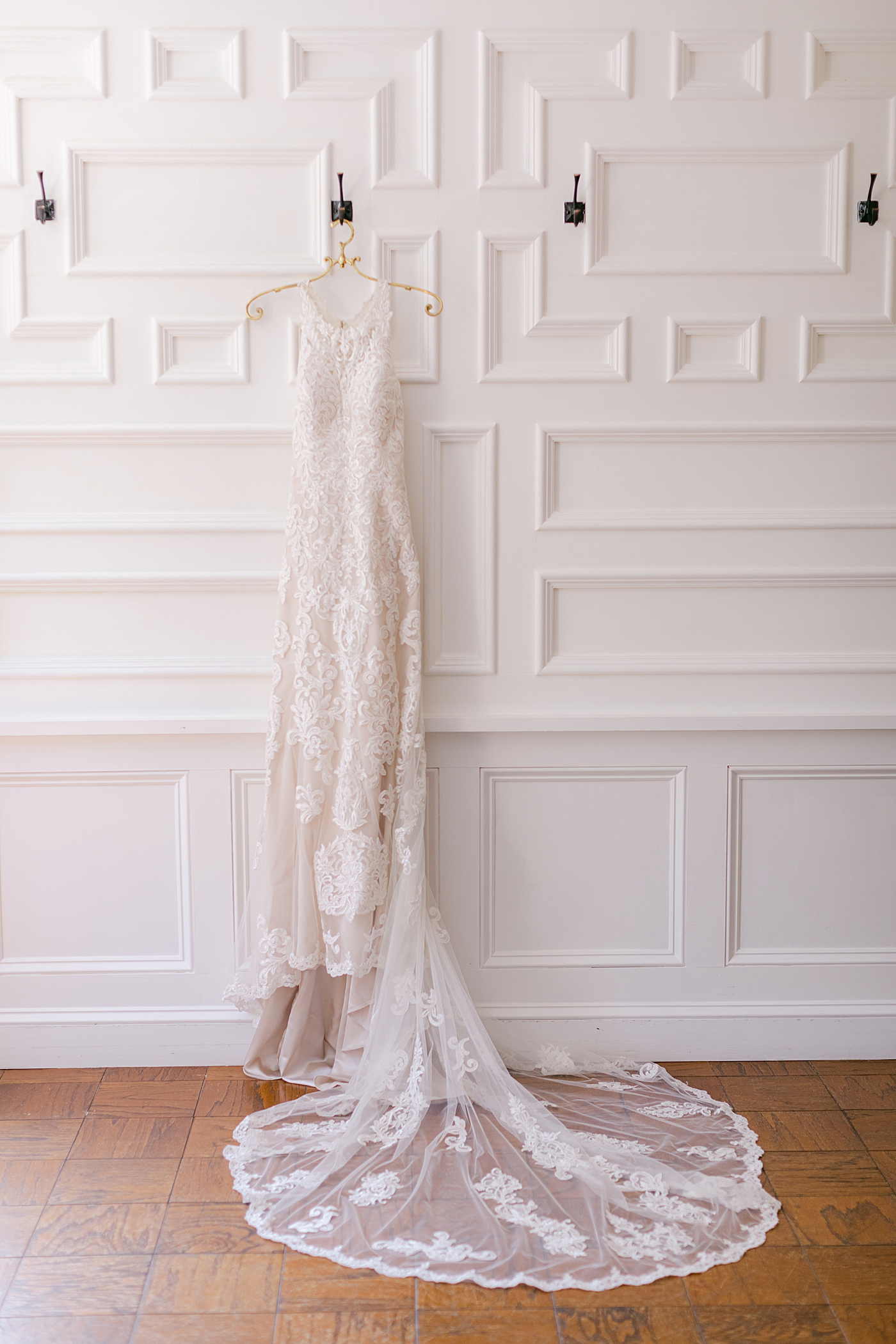 Bridal gown hanging on a white wall during Hotel du Village Wedding | Image by Hope Helmuth Photography