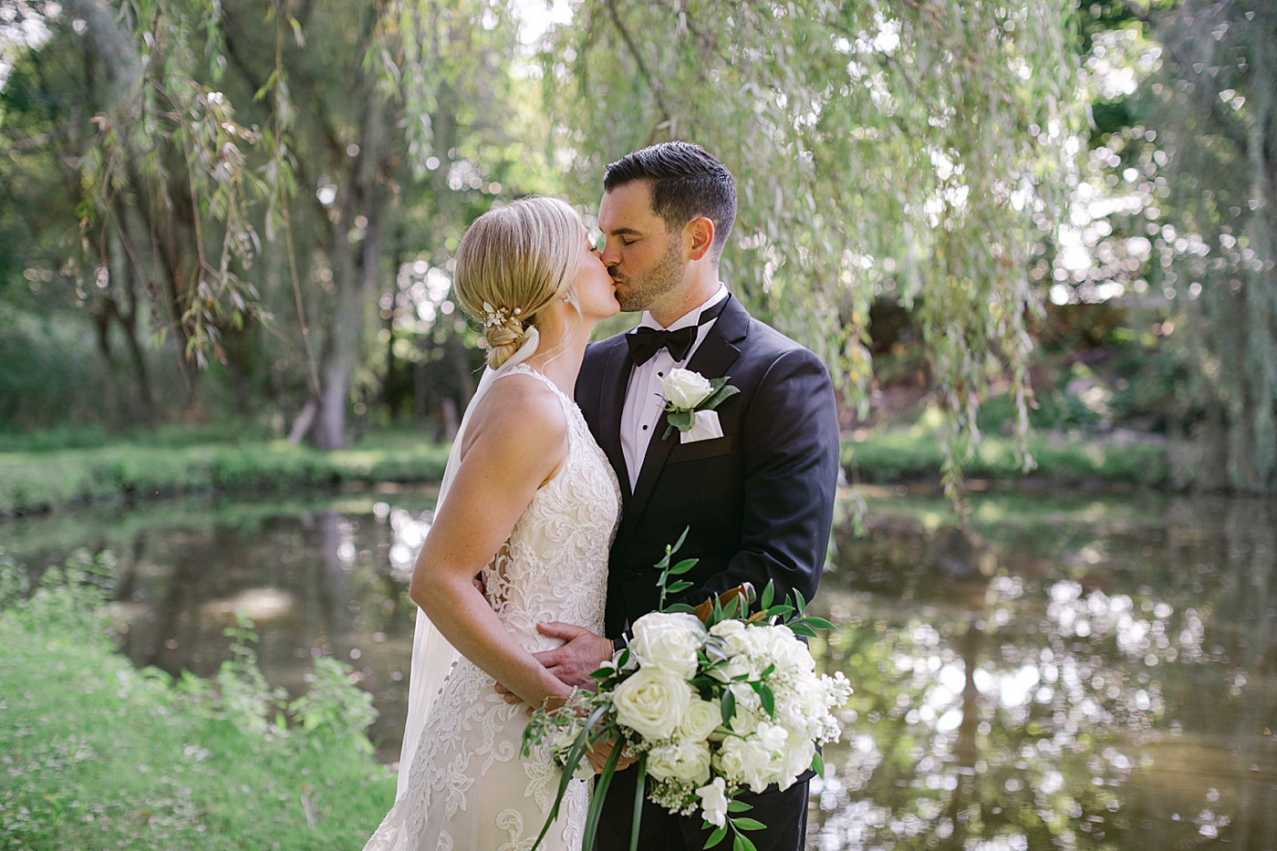 Bride and groom kissing near a pond during Hotel du Village Wedding | Image by Hope Helmuth Photography