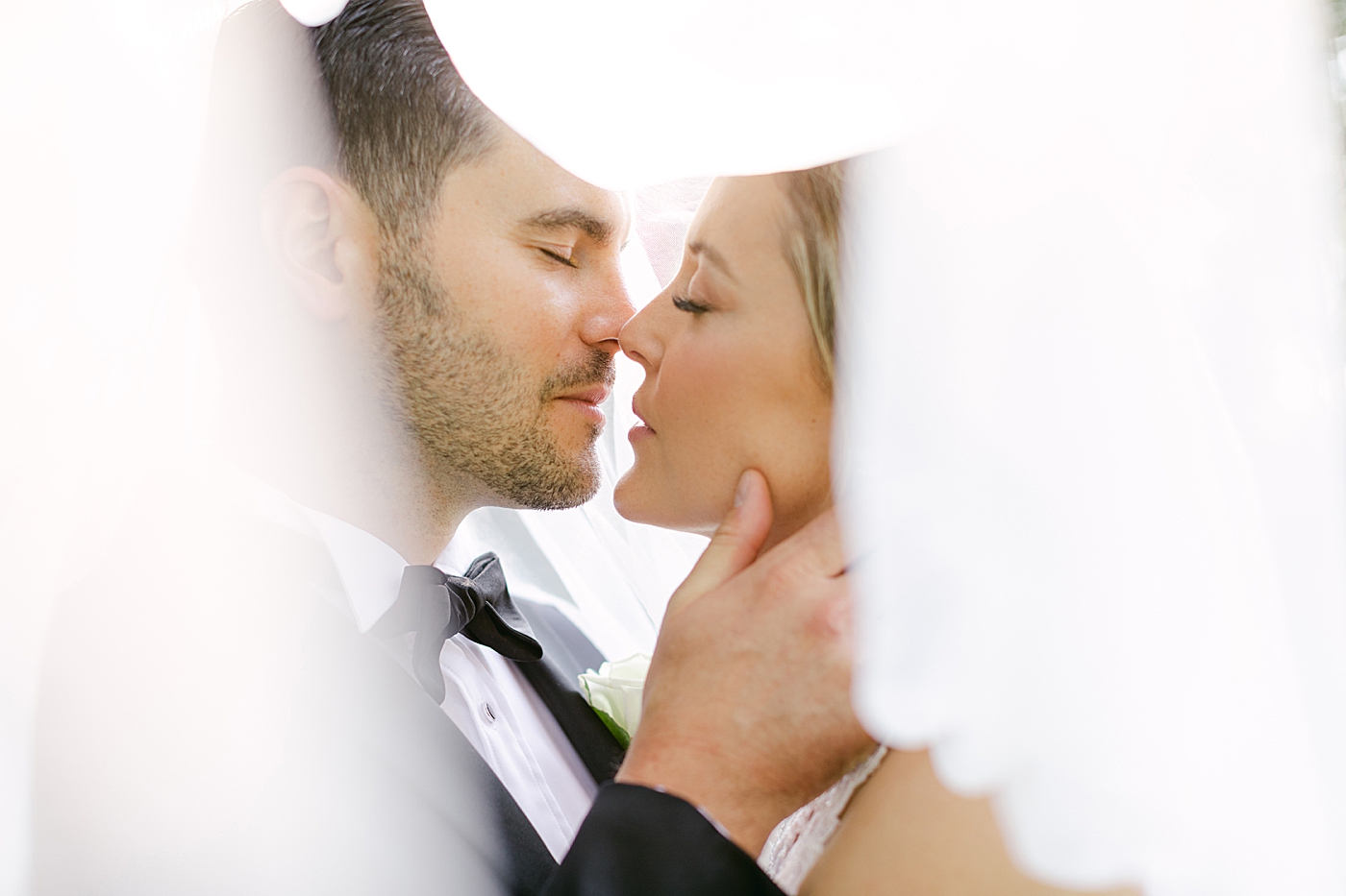 Bride and groom kissing under veil during Hotel du Village Wedding | Image by Hope Helmuth Photography