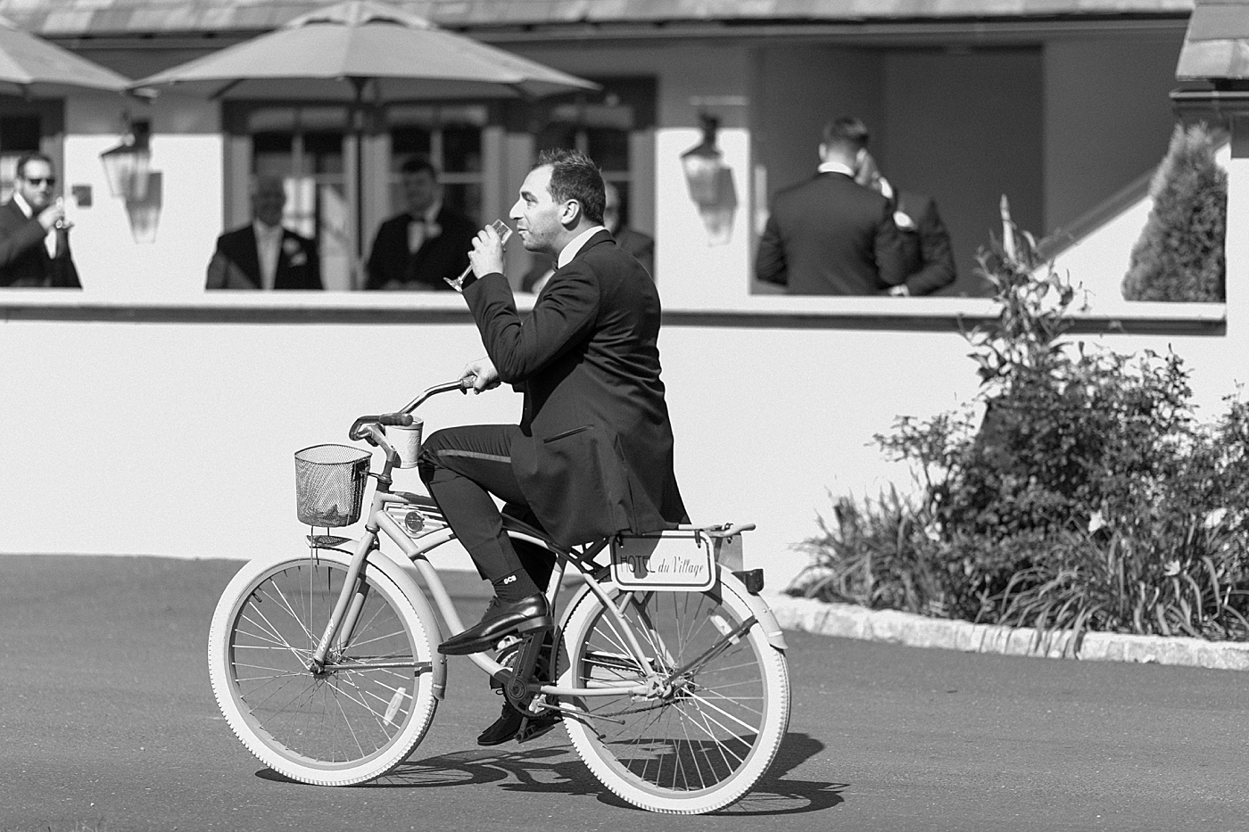 Wedding guest drinking wine ridding a bike during Hotel du Village Wedding | Image by Hope Helmuth Photography