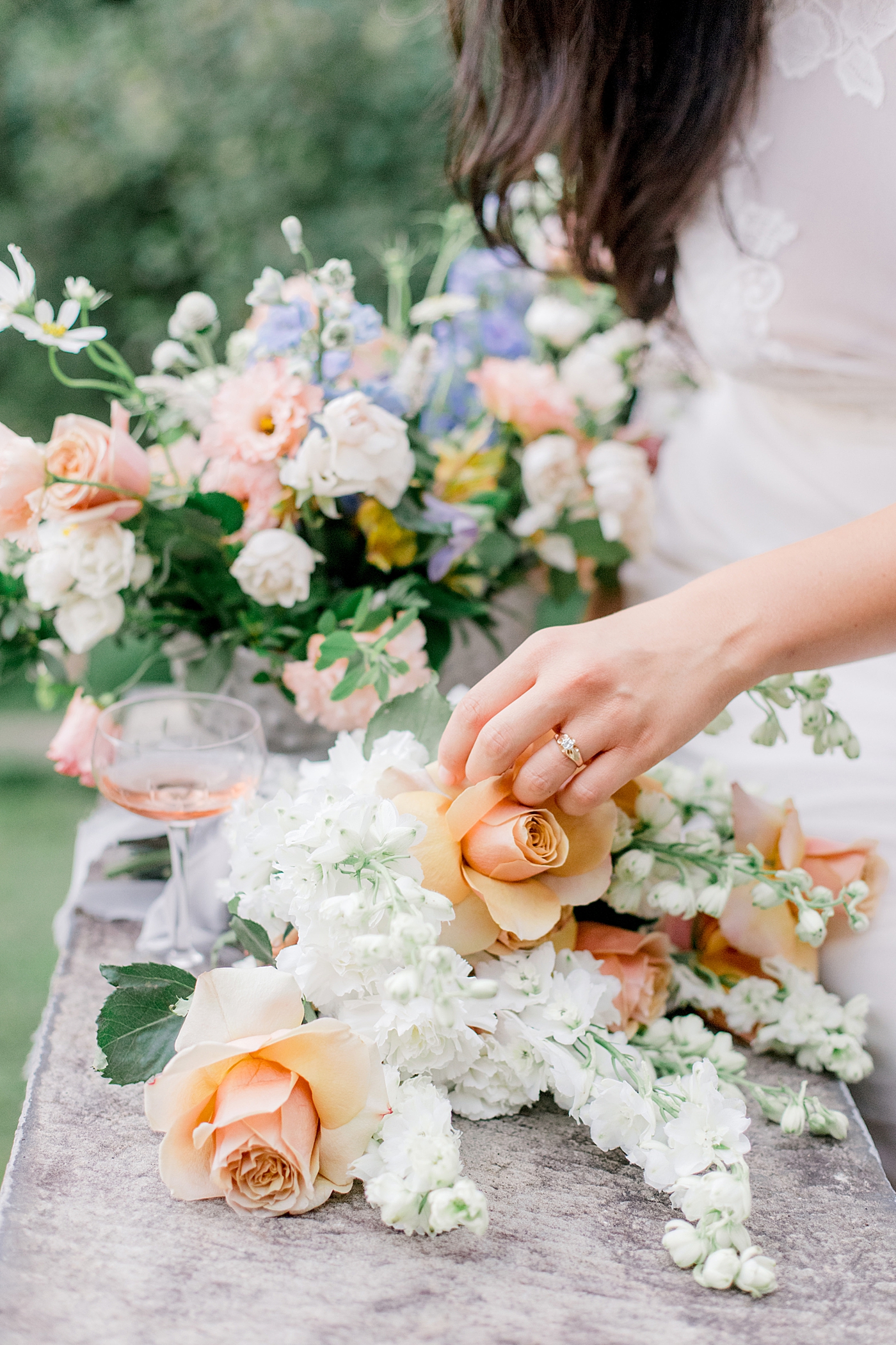Bride in a white lace dress adjusting her bouquet with peach roses | Image by Hope Helmuth Photography