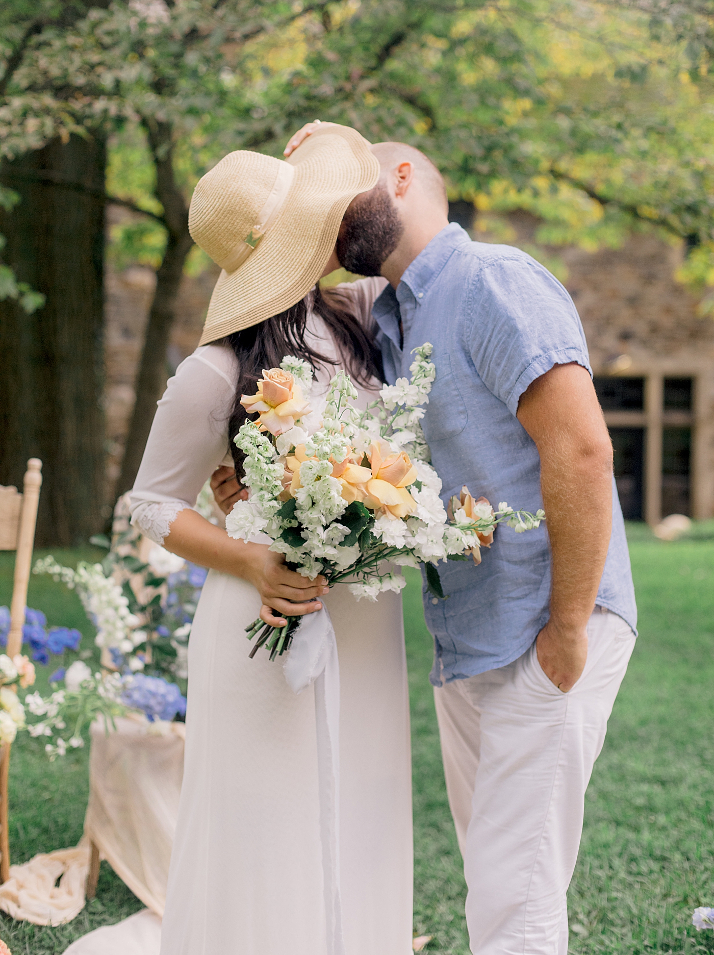 Bride holding a bouquet and wearing a hat kissing her groom | Image by Hope Helmuth Photography
