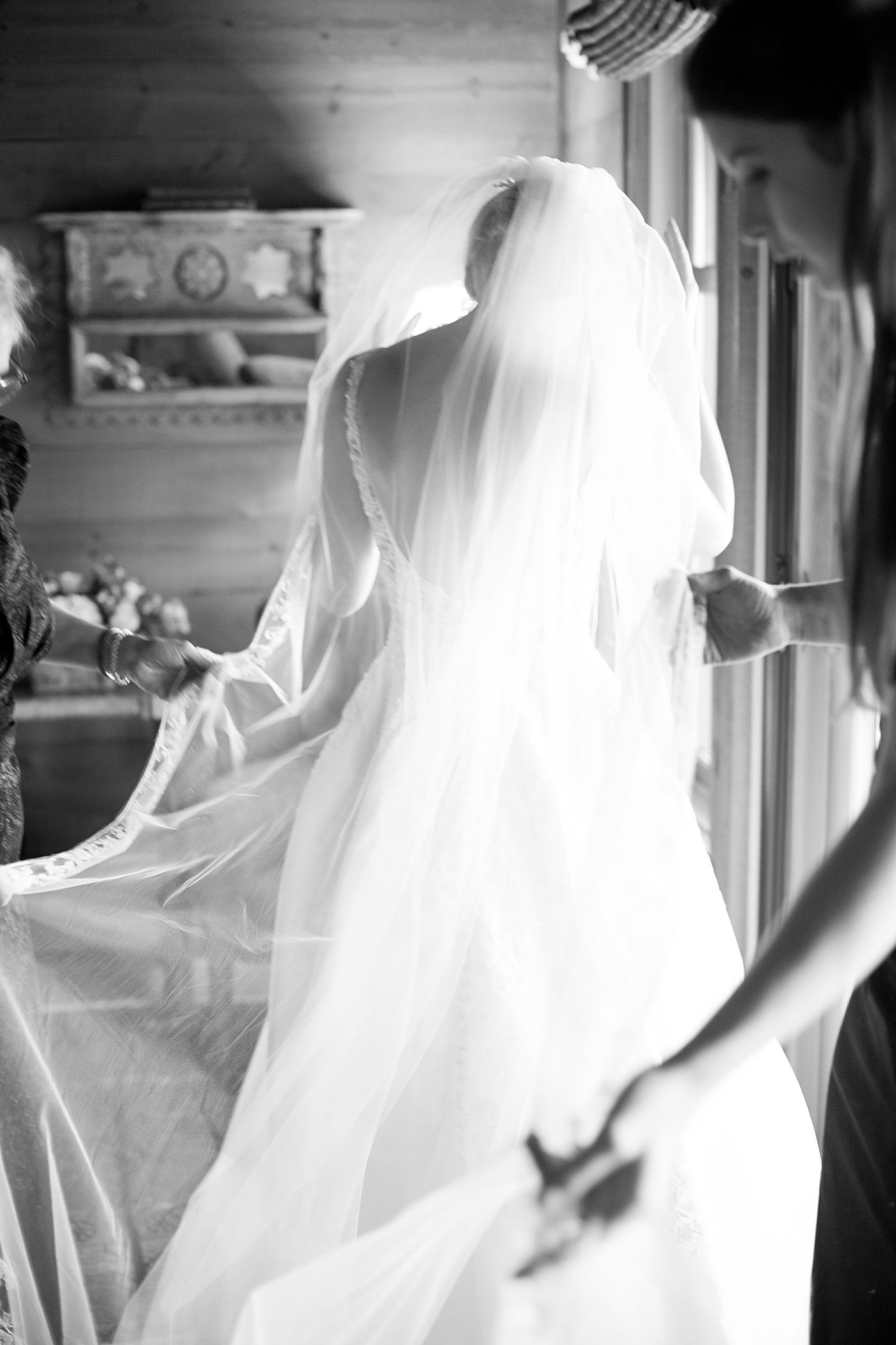 Black and white image of bride being helped into her gown | Image by Hope Helmuth Photography