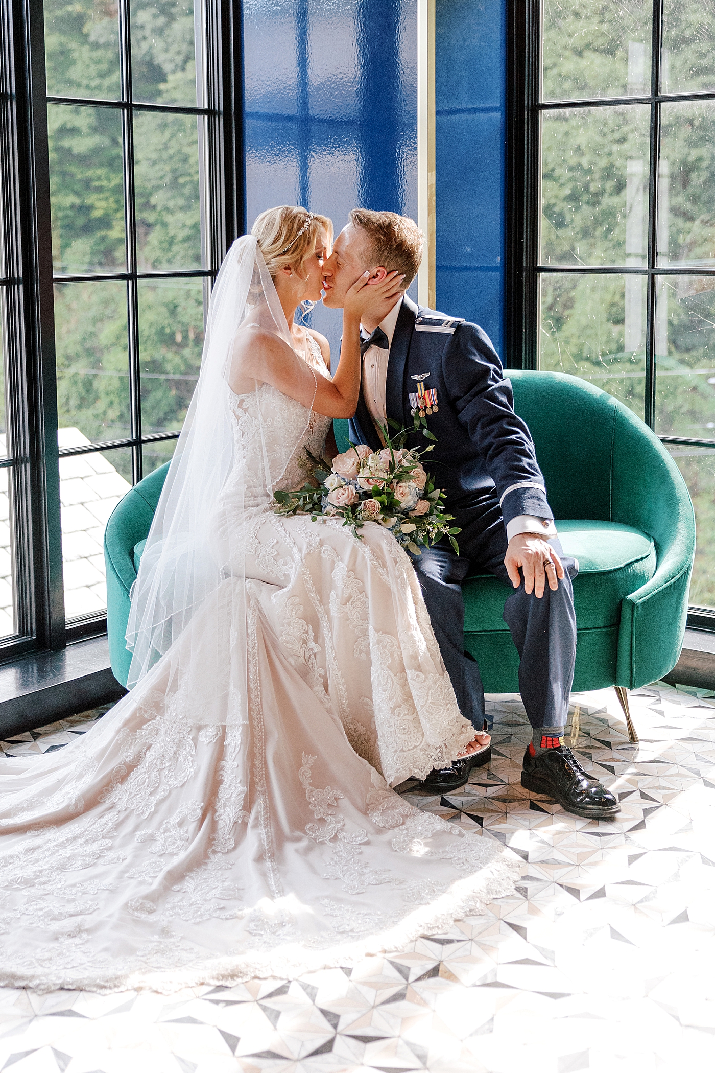 Bride and groom kiss sitting on a green sofa during River House Odette's Wedding | Image by Hope Helmuth Photography