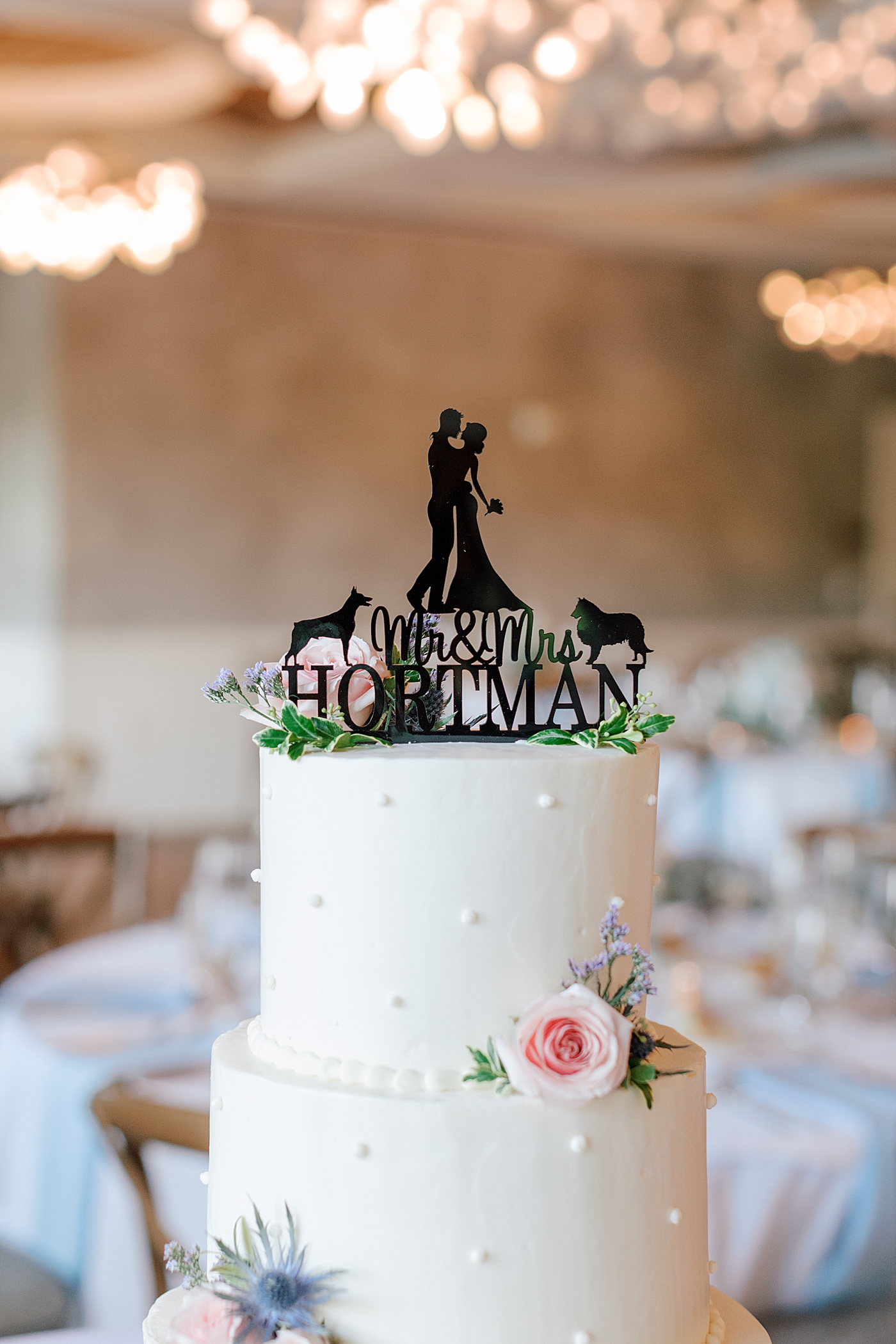 Wedding cake with flowers and black cake topper during River House Odette's Wedding | Image by Hope Helmuth Photography