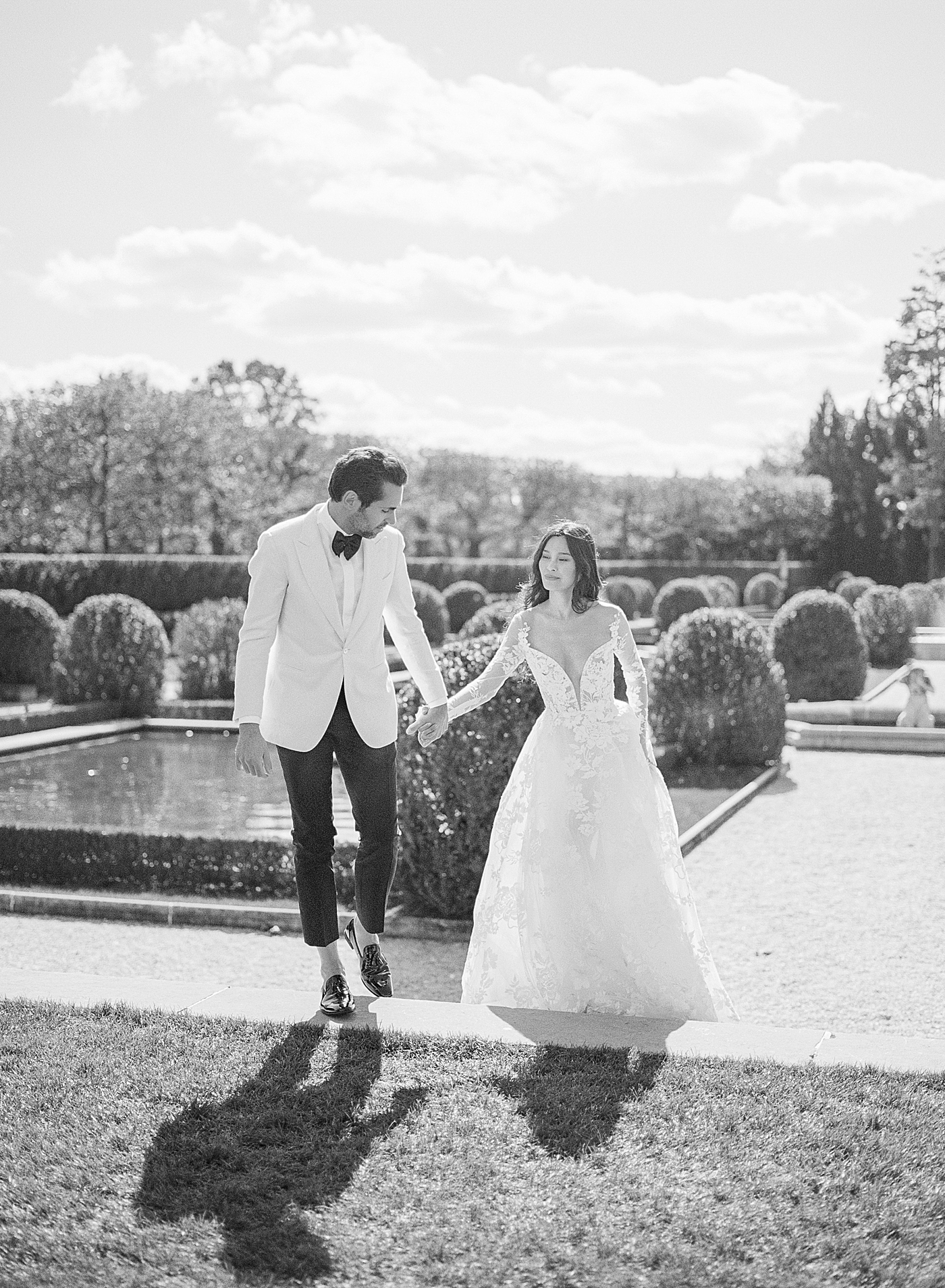 Black and white image of a bride and groom walking in a European garden | Image by Hope Helmuth Photography