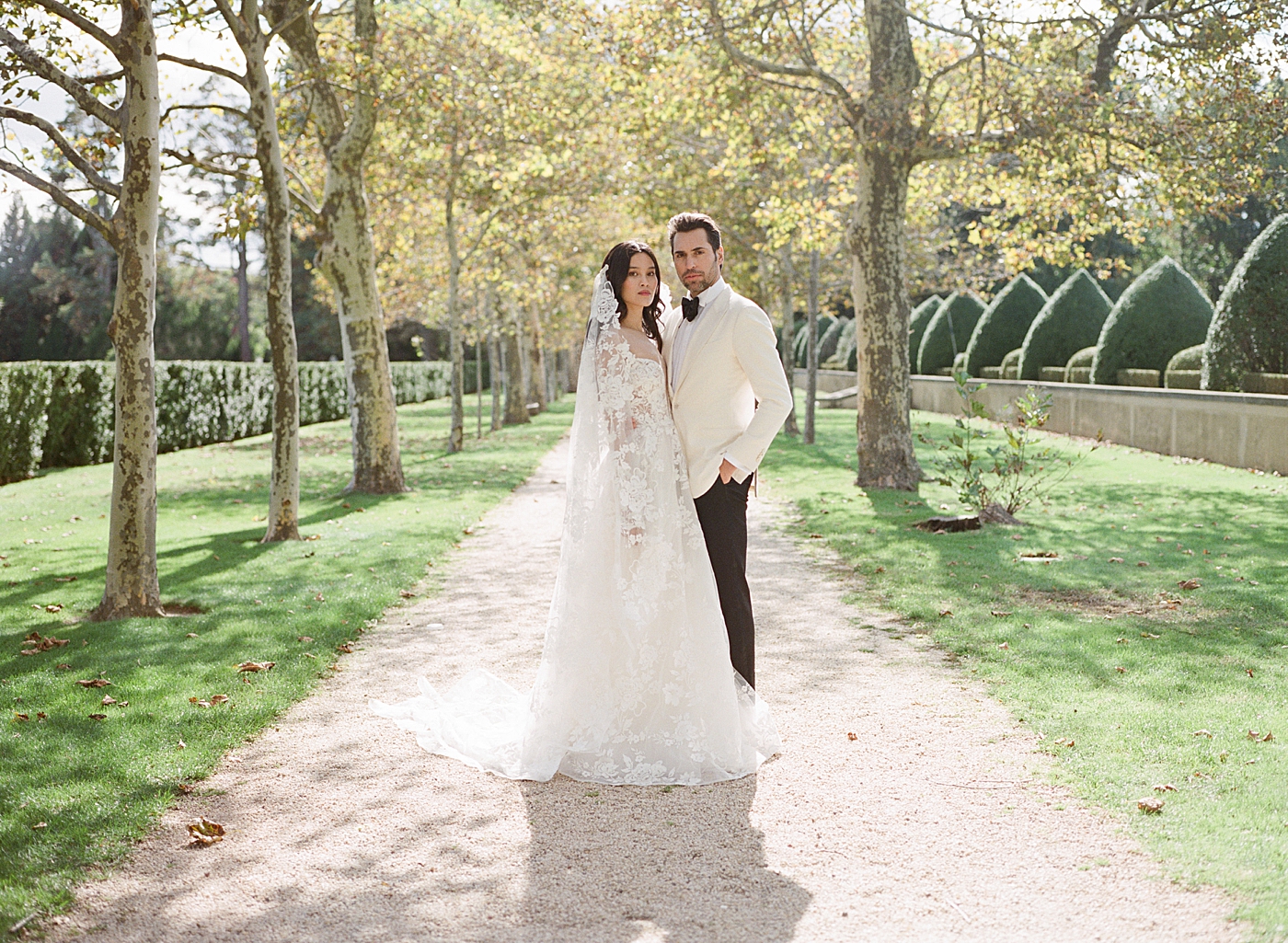 Portrait of bride and groom at the end of a tree-lined driveway during Oheka castle wedding | Image by Hope Helmuth Photography