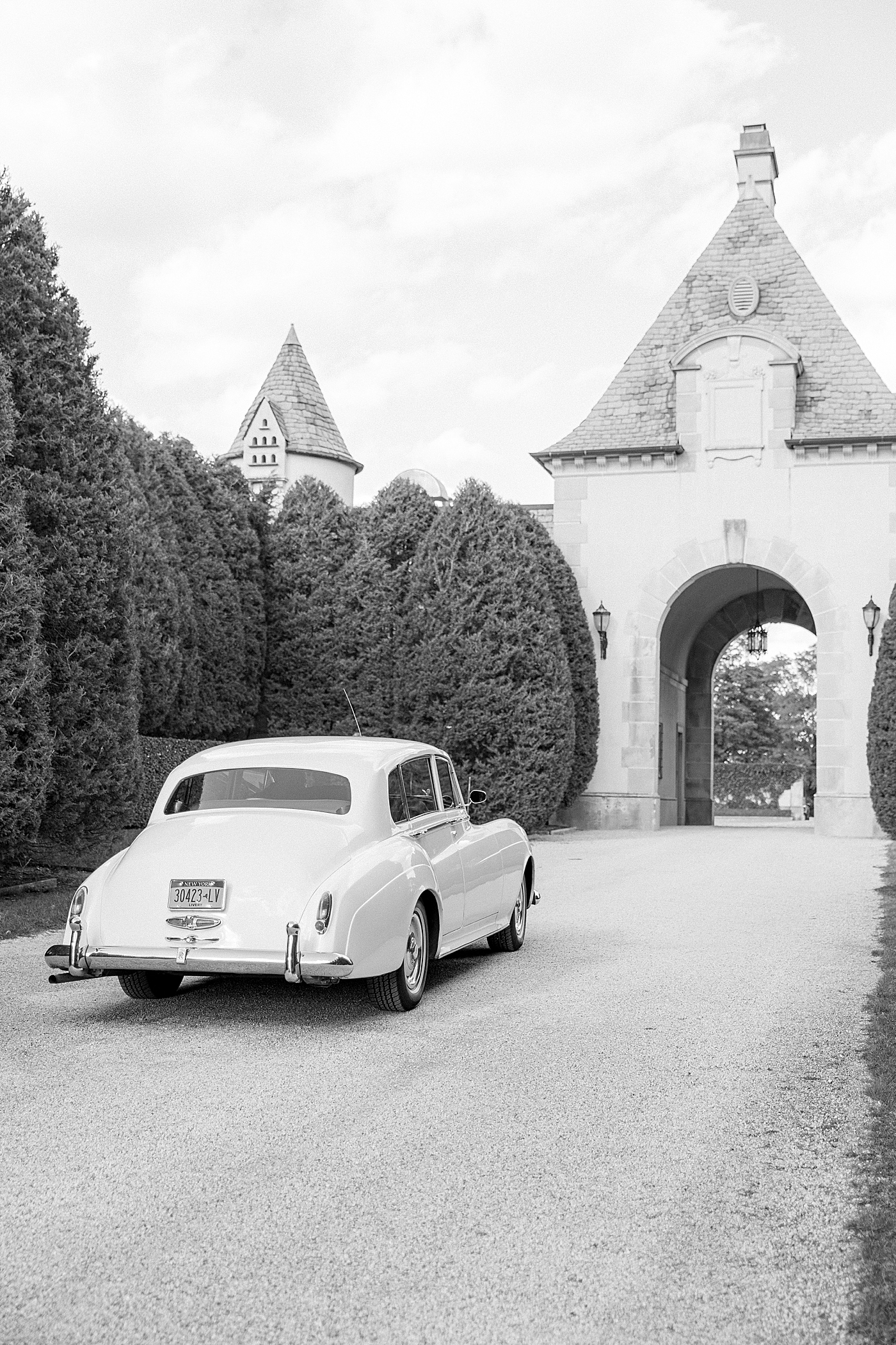 Black and white image of a classic car in a driveway during Oheka castle wedding | Image by Hope Helmuth Photography