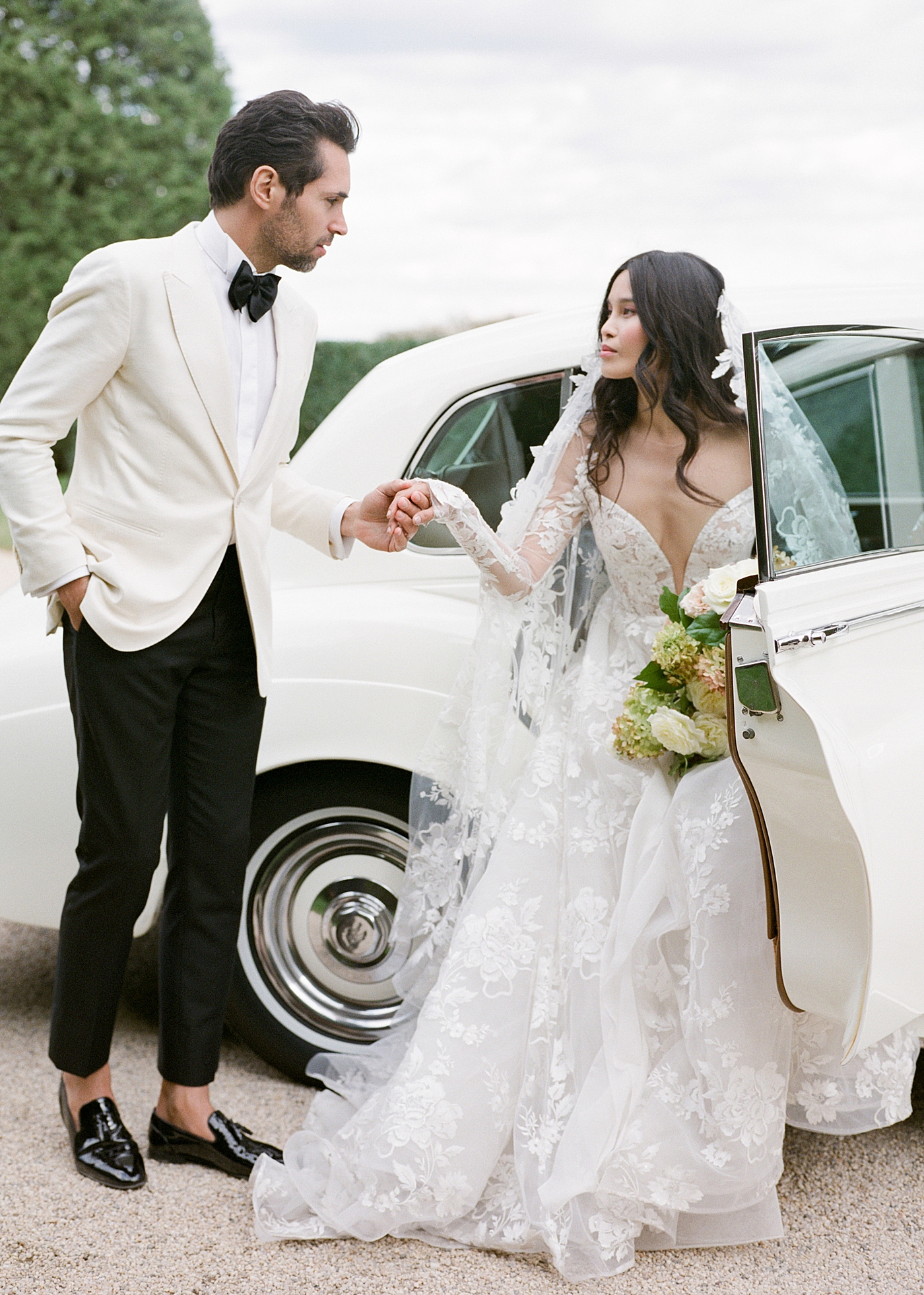 Bride and groom getting out of a classic car in a gravel driveway during Oheka castle wedding | Image by Hope Helmuth Photography