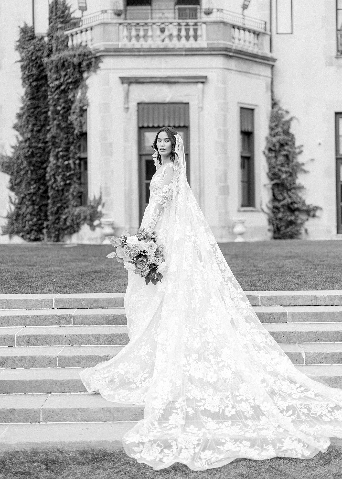 Black and white image of a bride in front of a grand entrance during Oheka castle wedding | Image by Hope Helmuth Photography