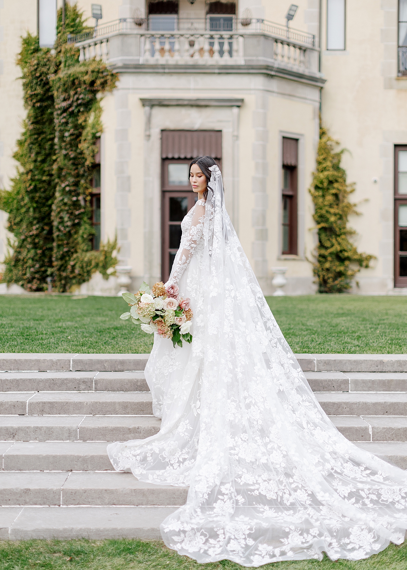 Bride with veil and bridal bouquet in front of a grand entrance during Oheka castle wedding | Image by Hope Helmuth Photography