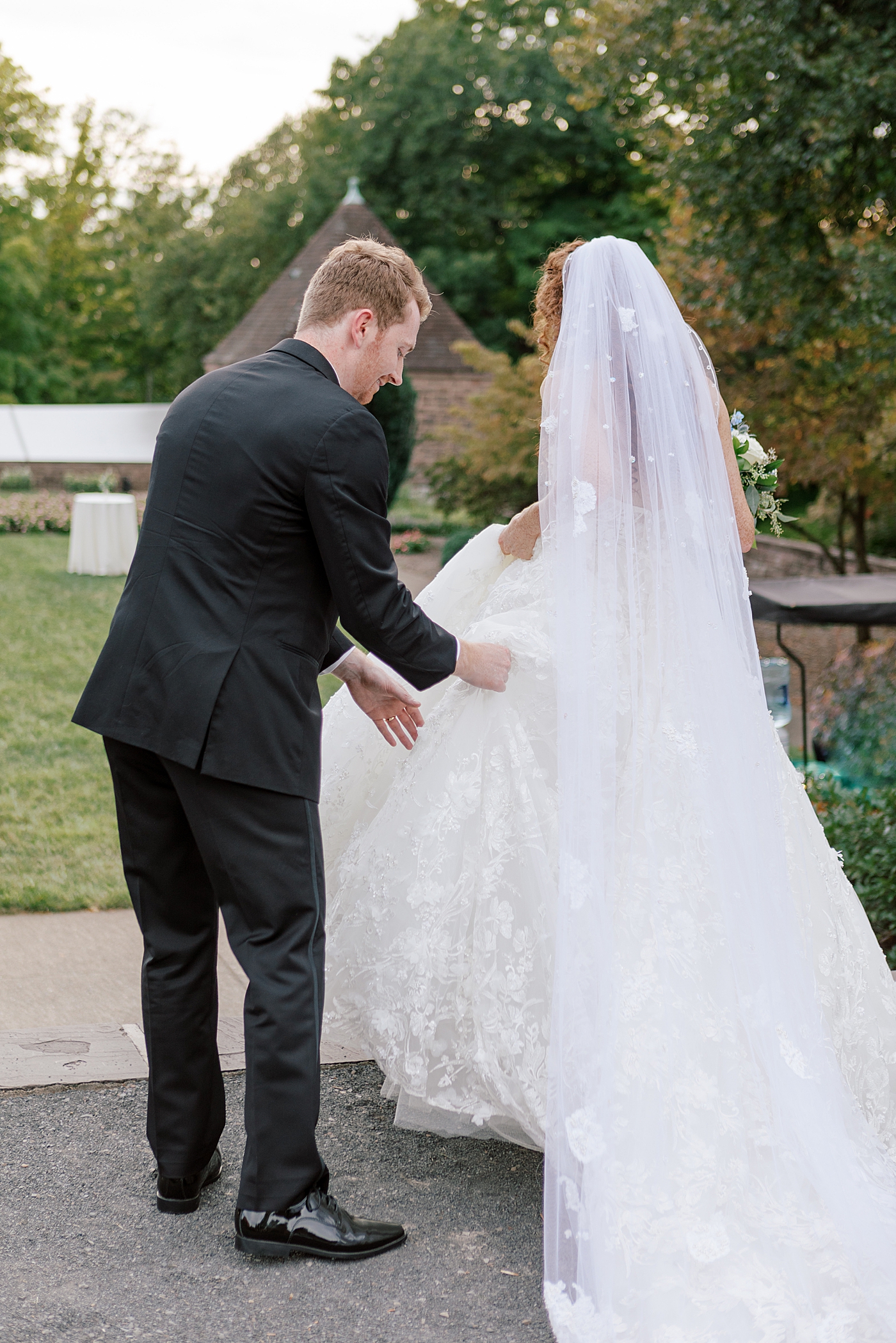 Groom helping bride with her dress during Tyler Gardens Wedding | Image by Hope Helmuth Photography