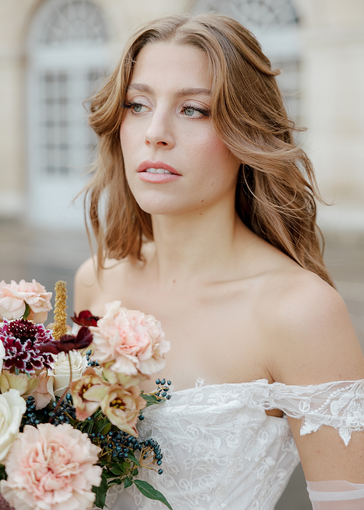 Close up of bride in an off the shoulder dress and white sheer gloves holding a wedding bouquet while looking out at a distance | Image by Hope Helmuth Photography