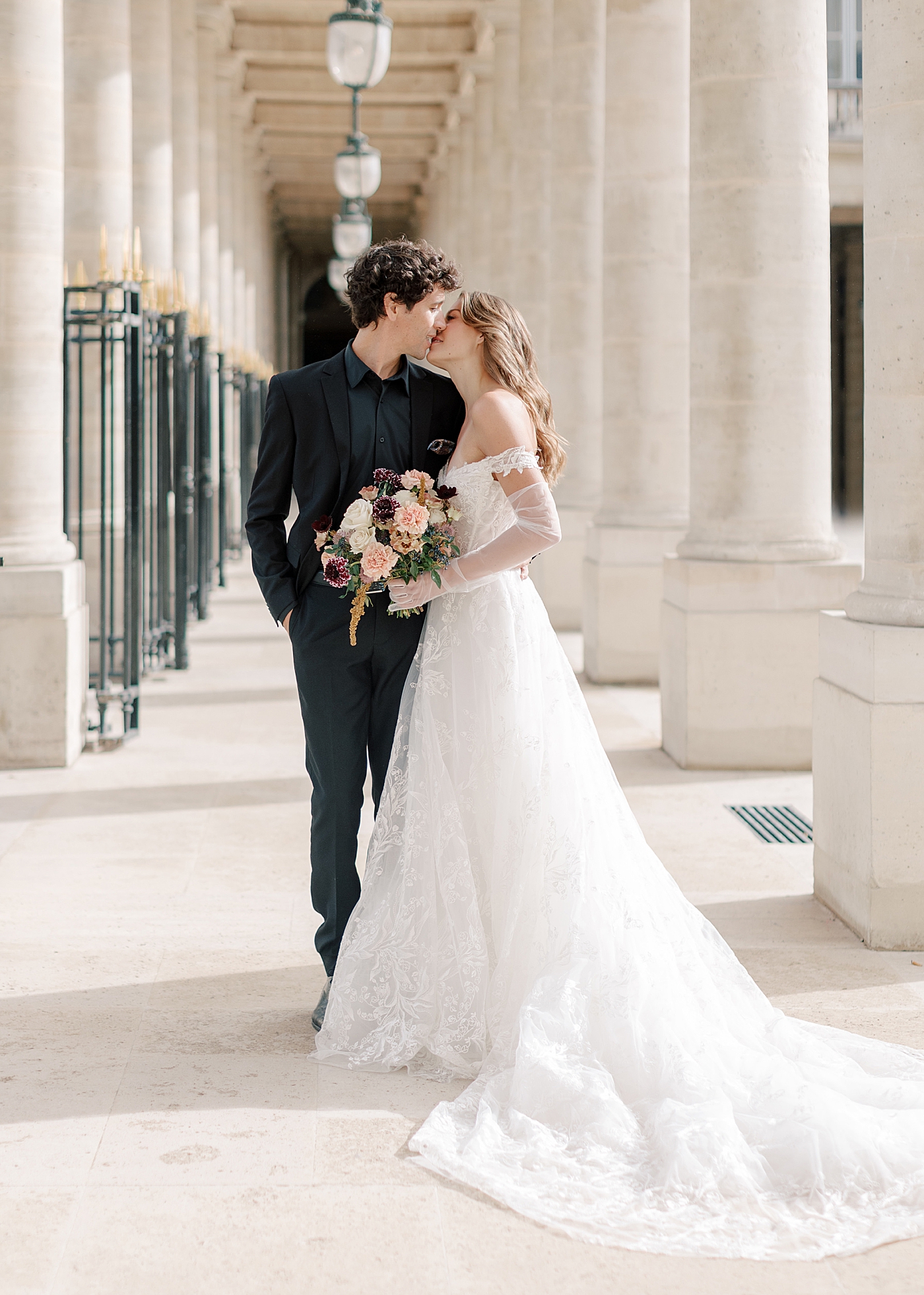 Image of a bride and groom embracing and kissing in an outdoor, sunlit, concrete corridor | Image by Hope Helmuth Photography
