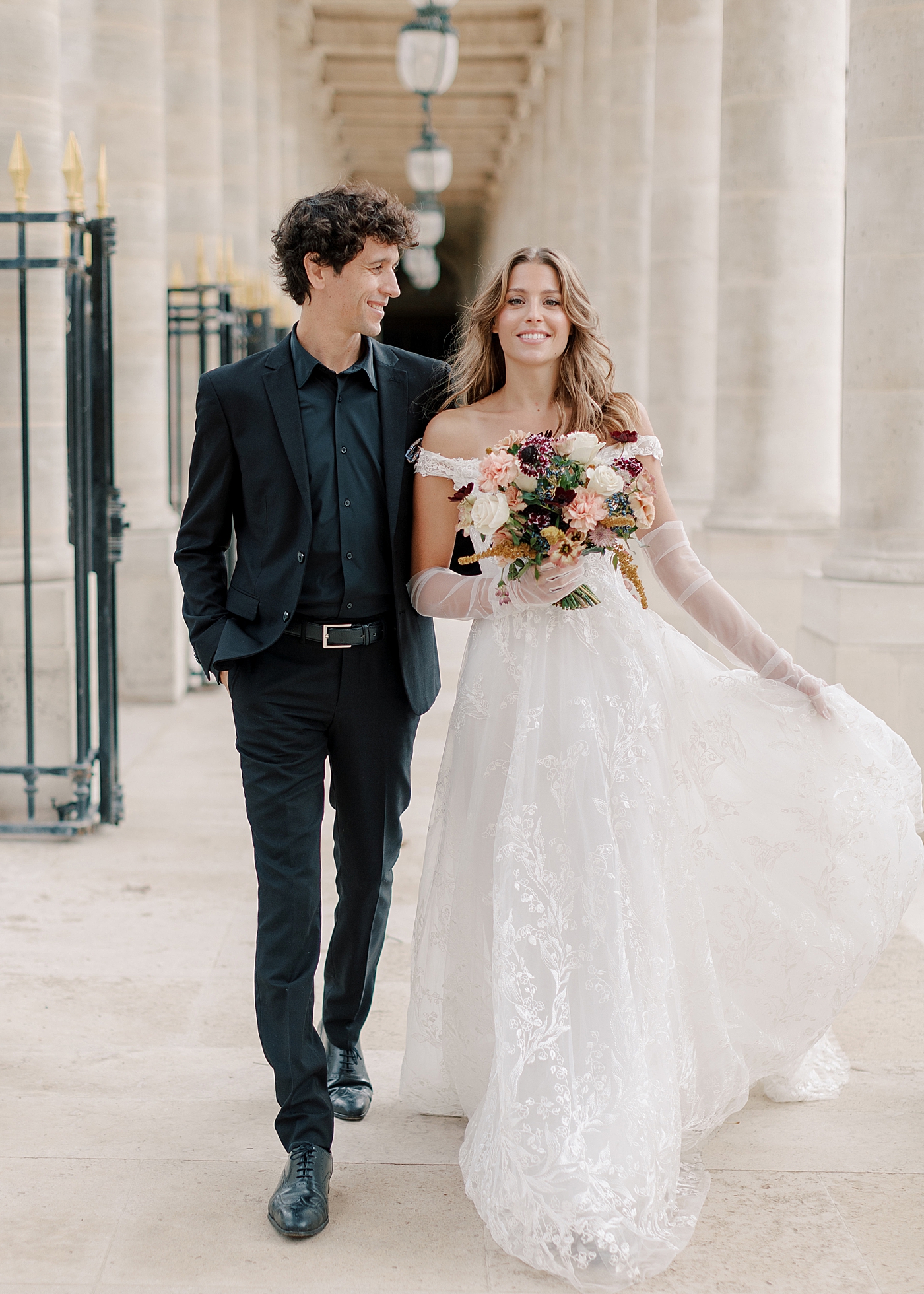 Image of a bride and groom embracing and walking towards the camera in an outdoor, sunlit, concrete corridor | Image by Hope Helmuth Photography