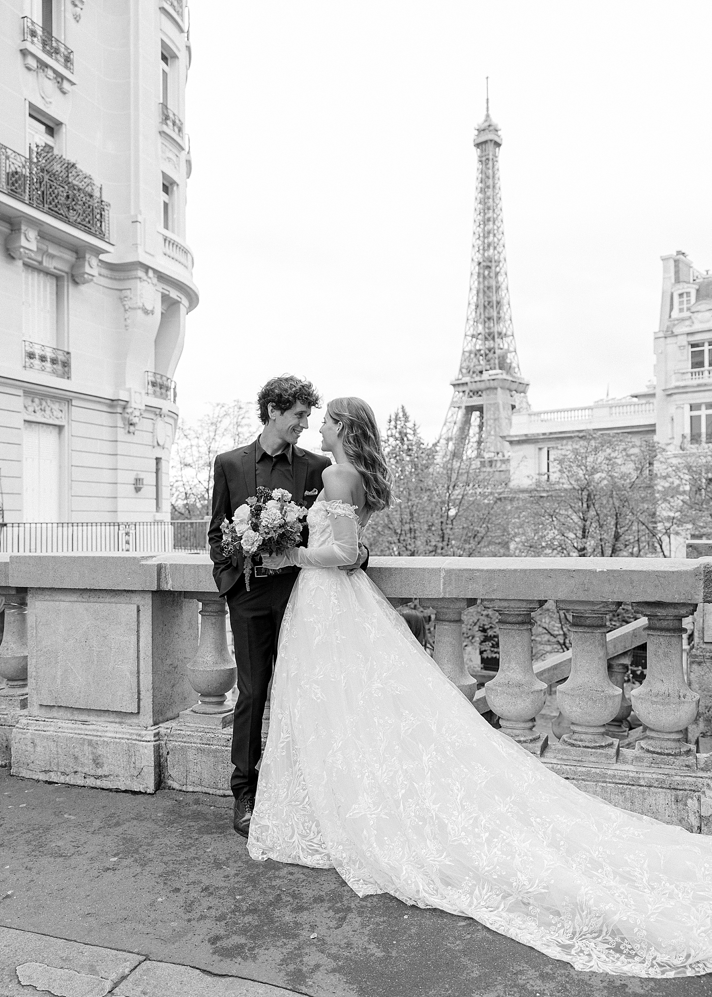 Black and white image of a bride and groom embracing in Paris with the Eiffel tower in the background | Image by Hope Helmuth Photography