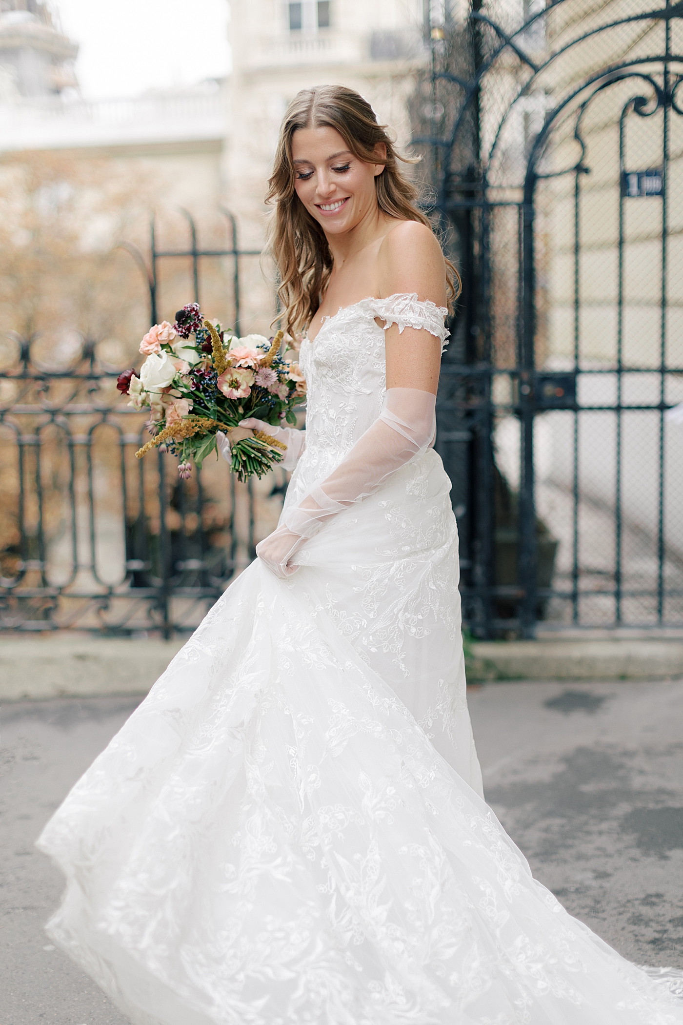 Bride holding a bouquet and twirling her dress on a street in Paris in front of an iron gate | Image by Hope Helmuth Photography