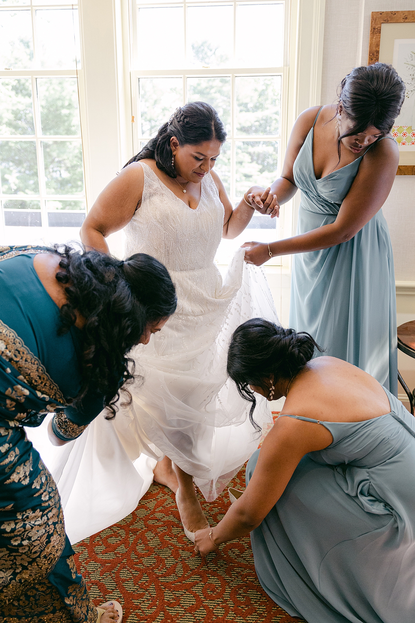Bridesmaids helping a bride into her wedding dress | Image by Hope Helmuth Photography