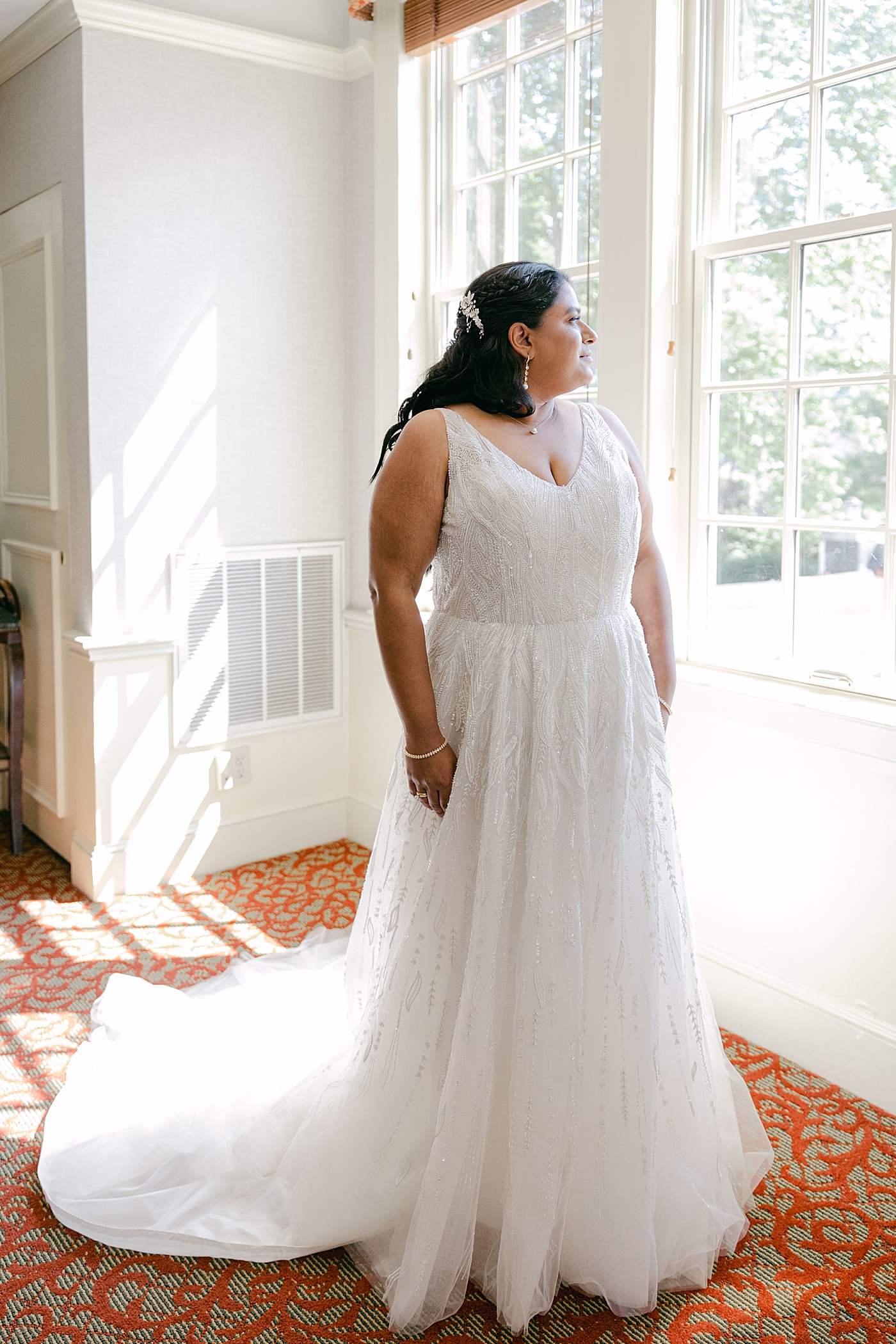 Bride in her wedding dress looking out a window on the right side of the image during Sagamore Wedding | Image by Hope Helmuth Photography