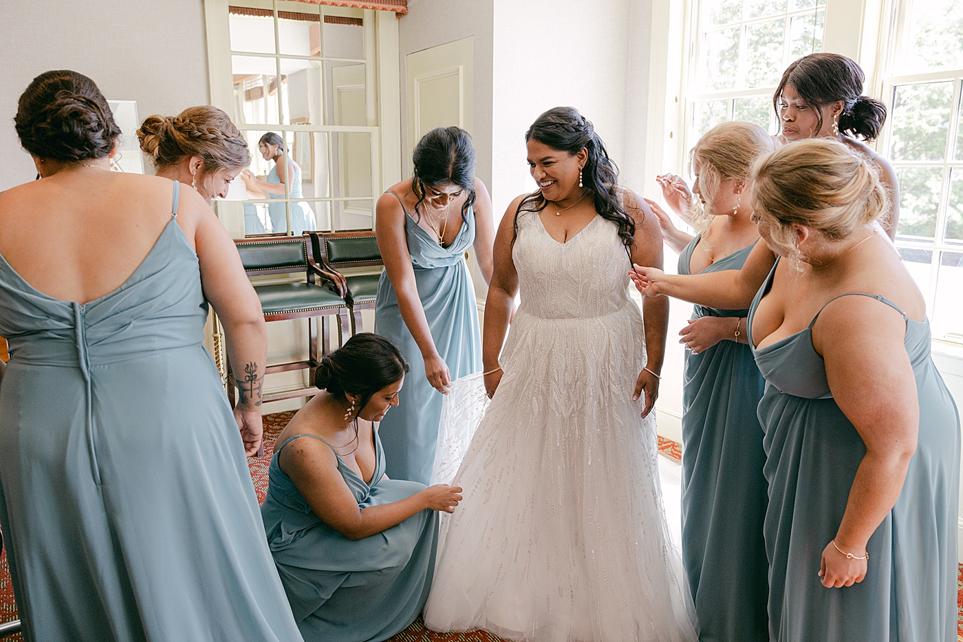 Bridesmaids helping a bride into her wedding dress during Sagamore Wedding | Image by Hope Helmuth Photography