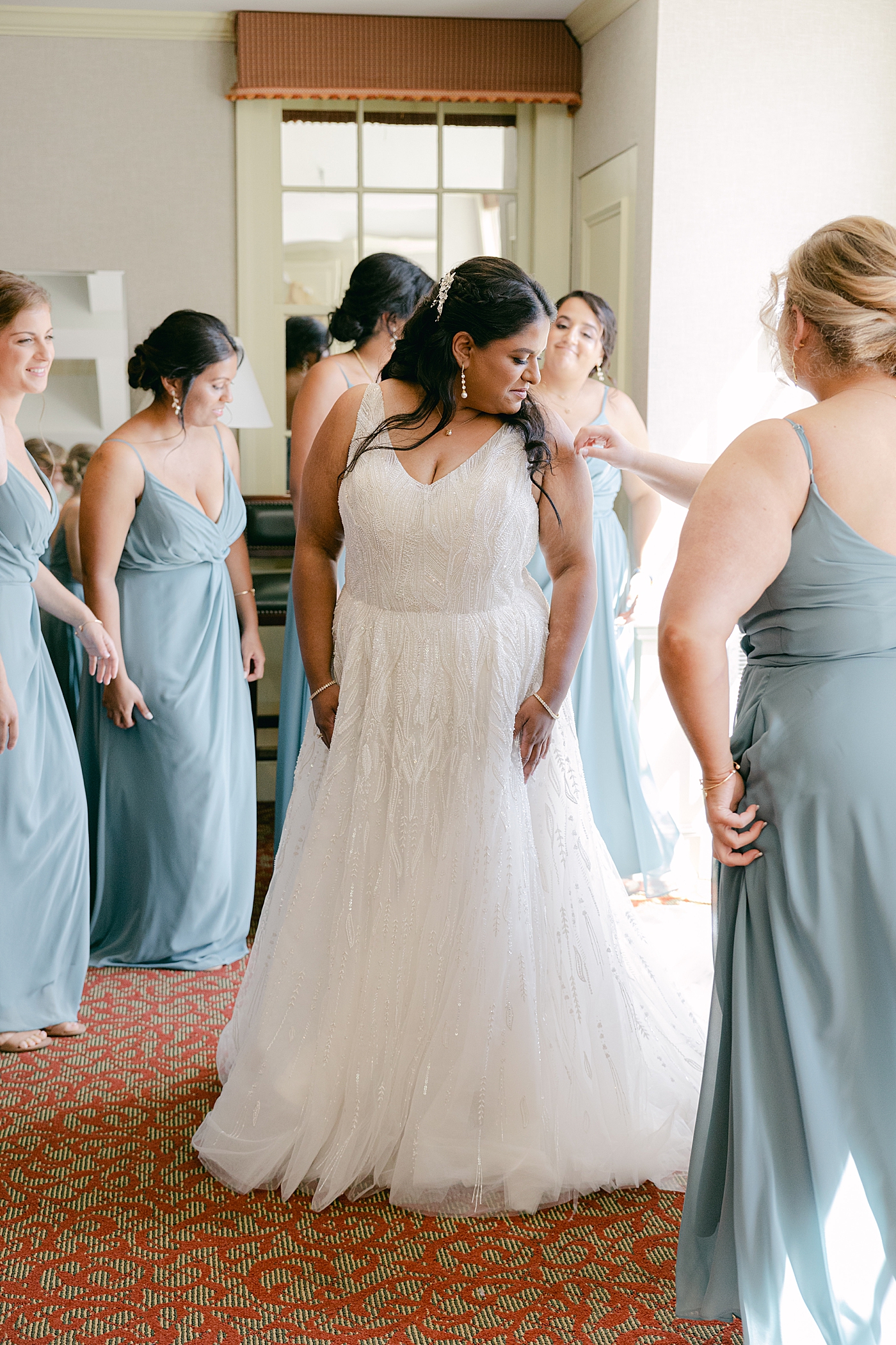 Bridesmaids helping a bride into her wedding dress | Image by Hope Helmuth Photography