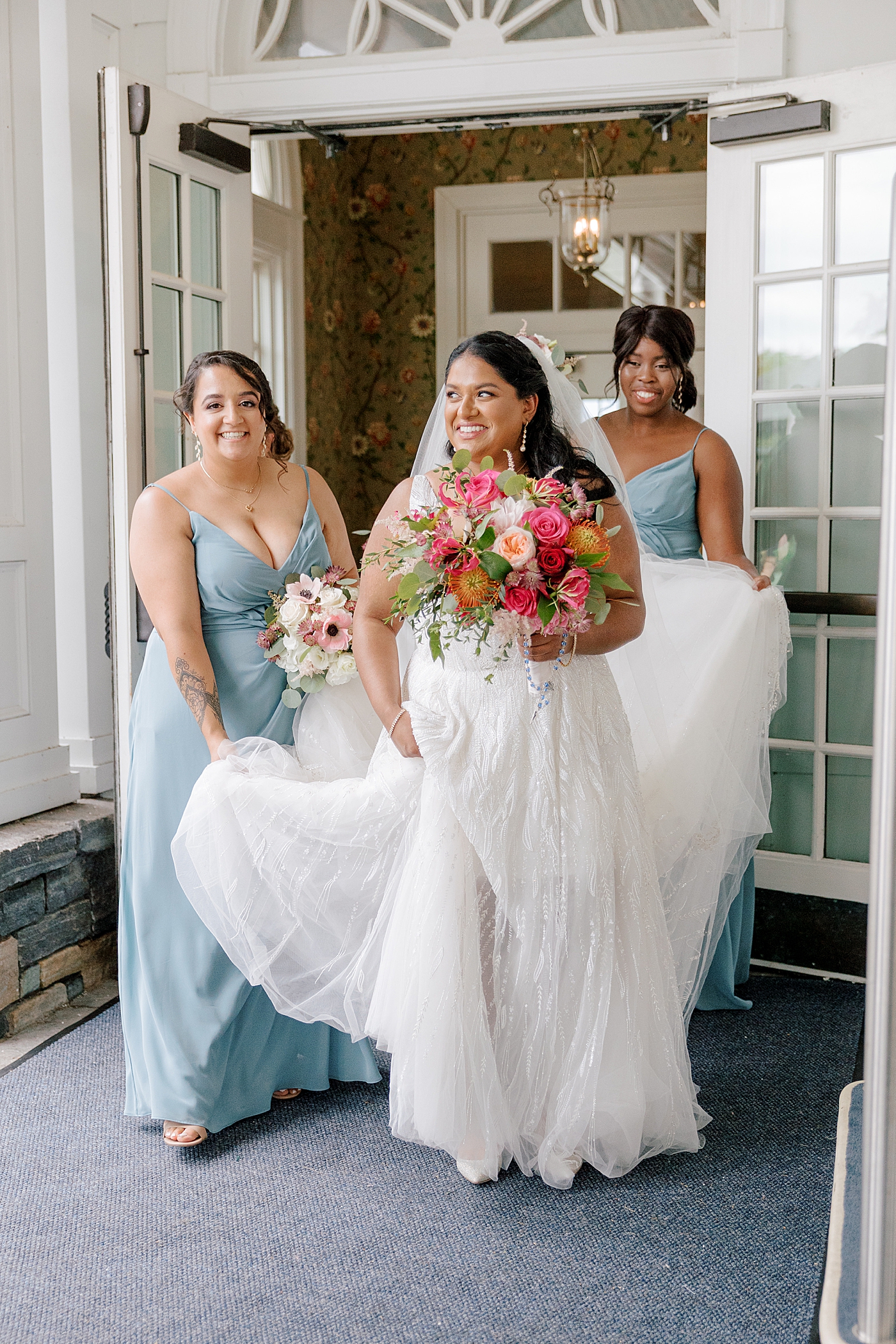 Bridesmaids helping a bride with colorful bridal bouquet walk in her dress | Image by Hope Helmuth Photography