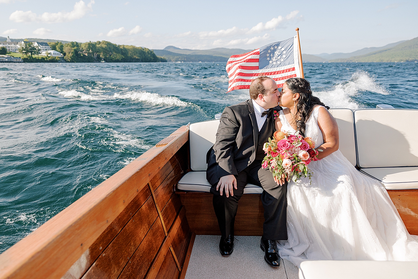 Bride and groom kissing in the back of a wooden boat with white cushions | Image by Hope Helmuth Photography