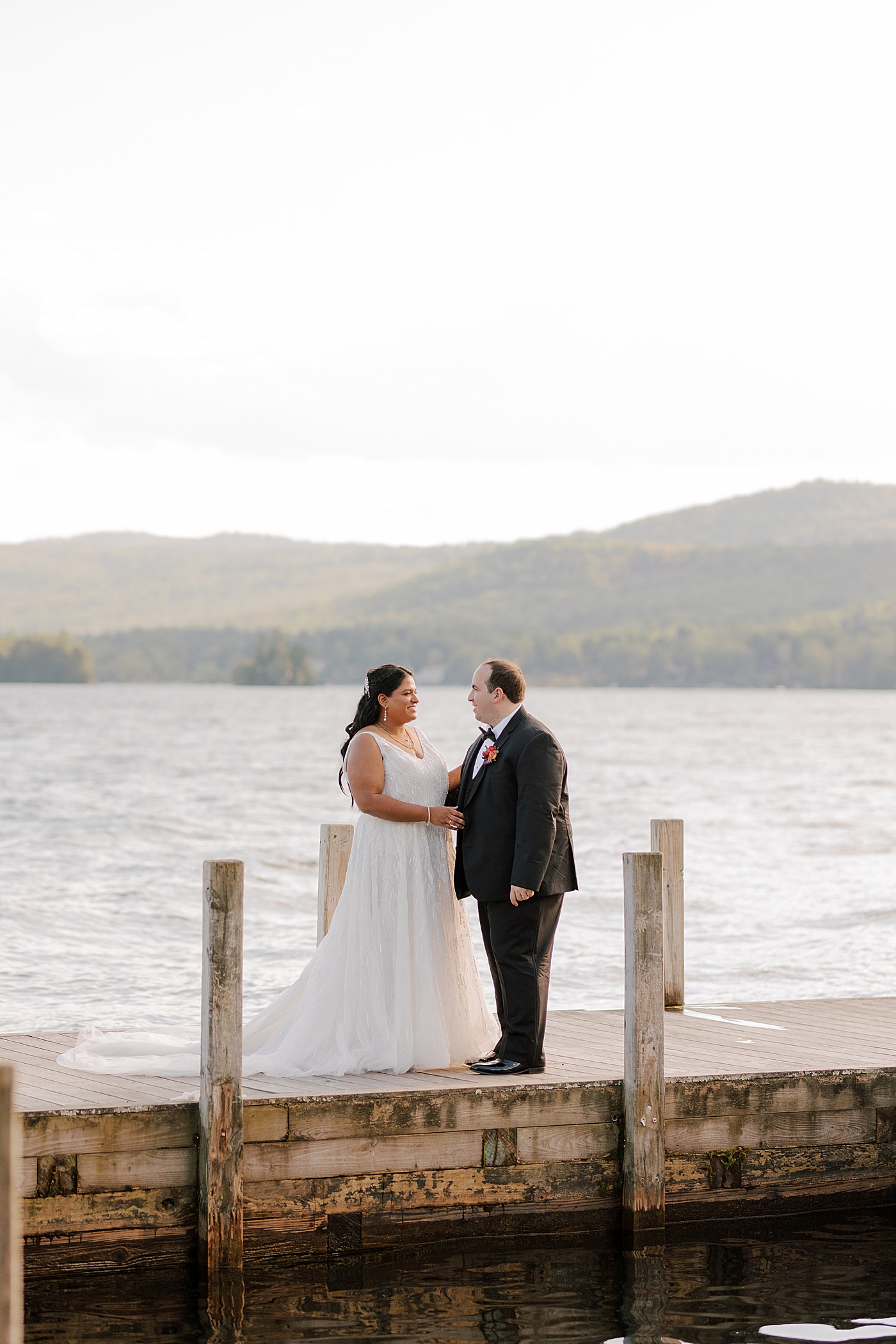 Bride and groom laughing together on a dock at sunset | Image by Hope Helmuth Photography