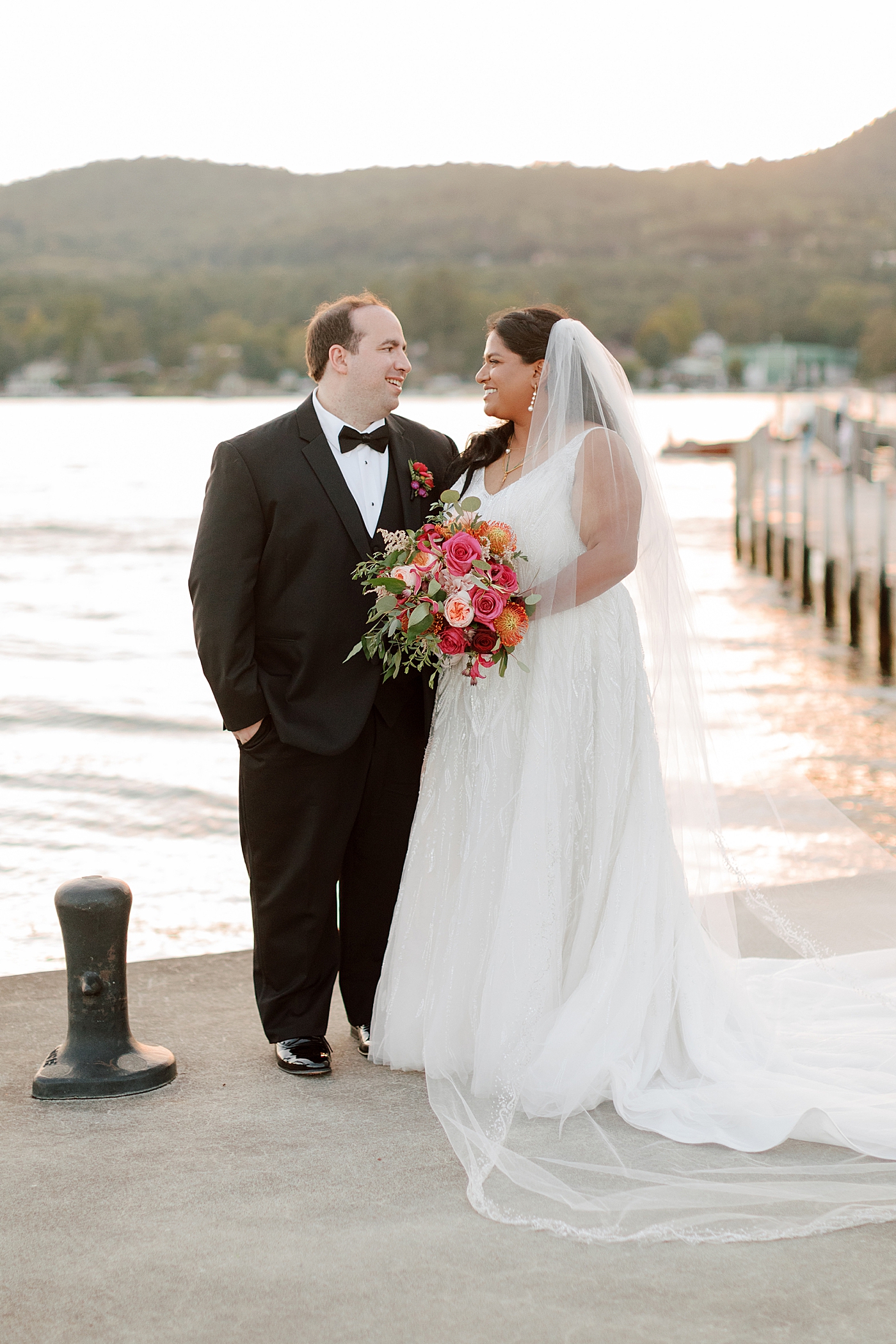 Bride and groom posing, smiling at each other on a dock at sunset | Image by Hope Helmuth Photography