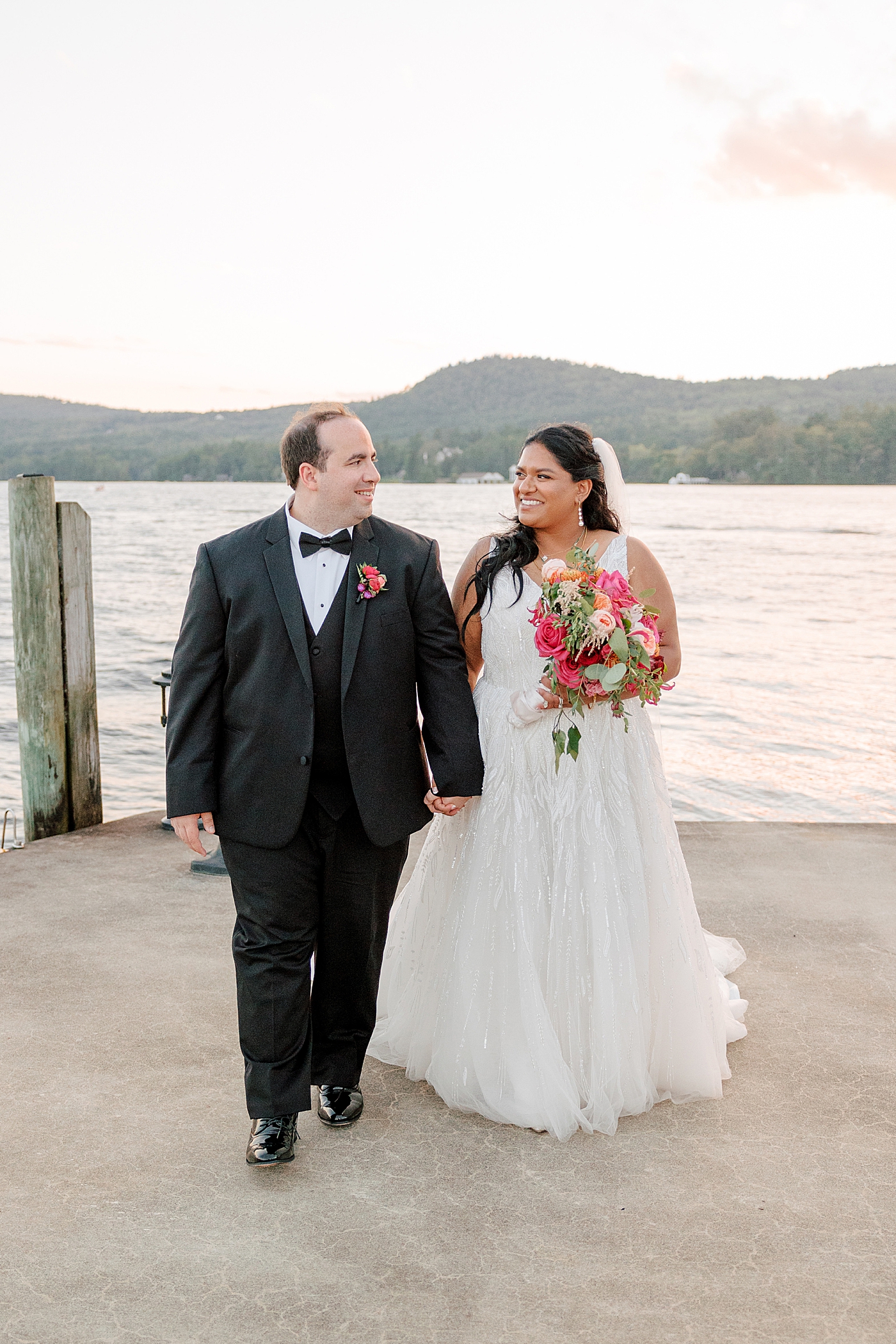 Bride and groom posing, smiling at each other on a dock at sunset during their Sagamore Wedding | Image by Hope Helmuth Photography