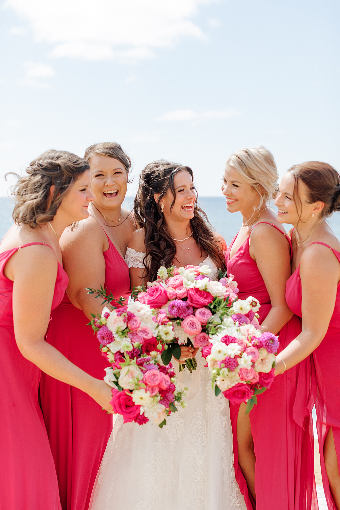Bride and bridesmaids in bright pink laughing at each other and holding colorful bouquets | Image by Hope Helmuth Photography