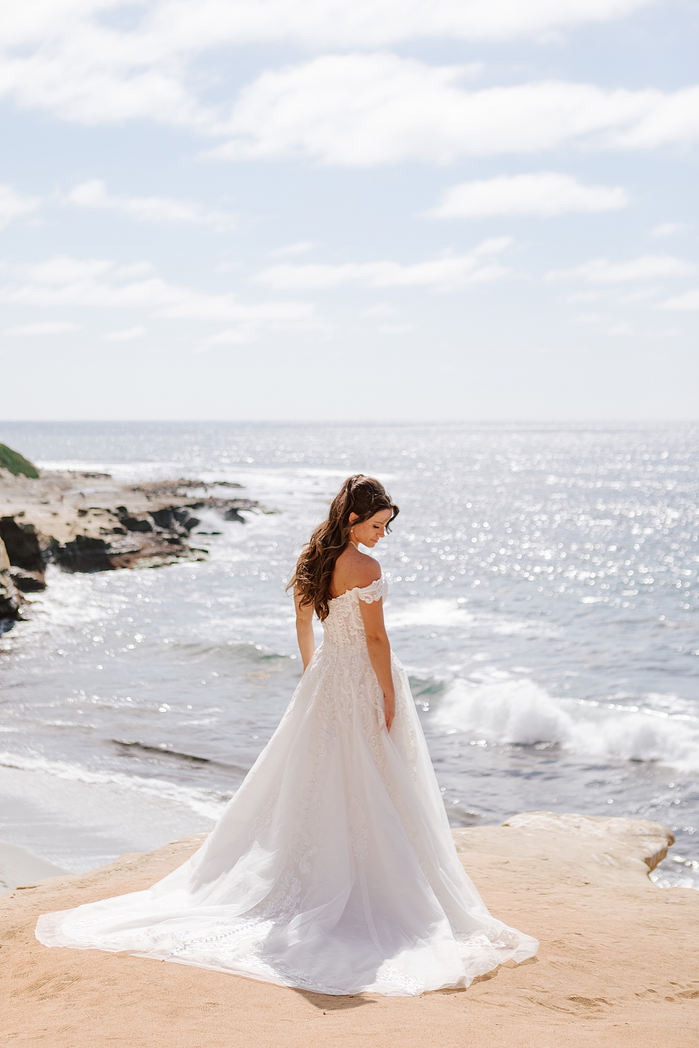 Bride looking over her shoulder in oceanfront, full length photo | Image by Hope Helmuth Photography