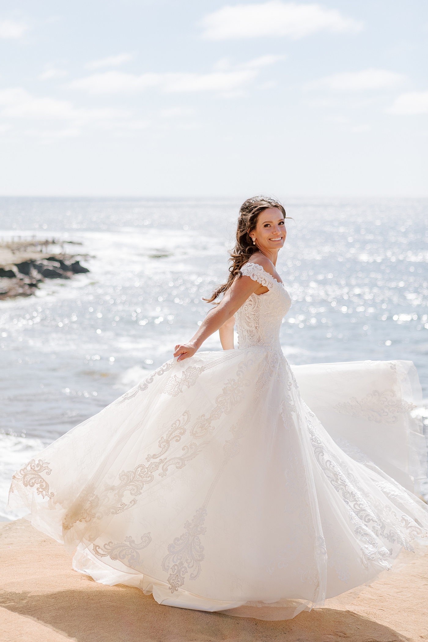 Bright photo of a bride ocean front looking at the camera while spinning in her dress | Image by Hope Helmuth Photography