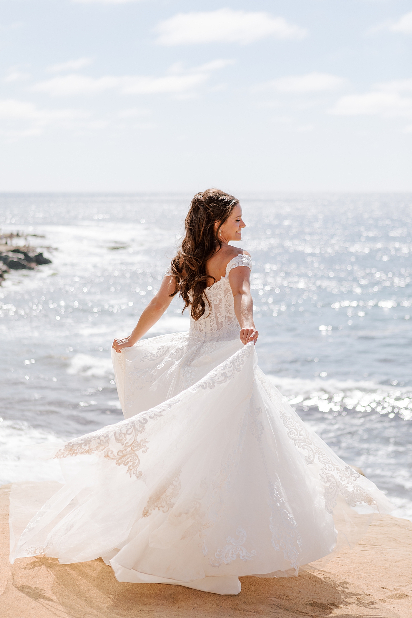 Bright photo of a bride ocean front looking at the camera while spinning in her dress | Image by Hope Helmuth Photography