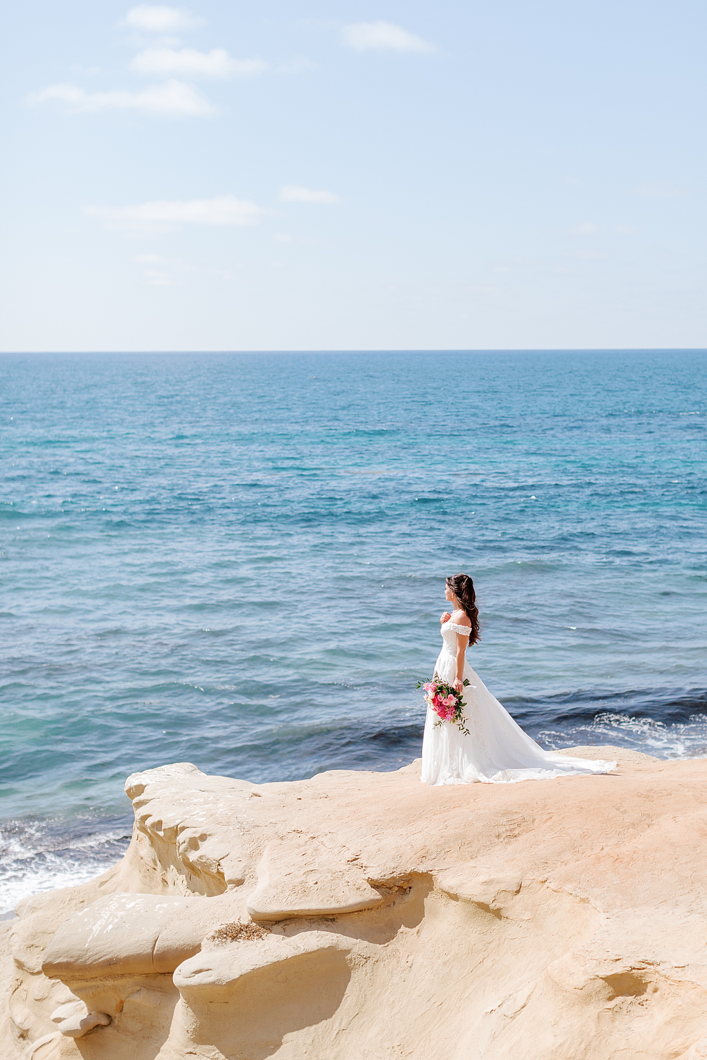 Bride alone at a distance looking away and out at the water | Image by Hope Helmuth Photography