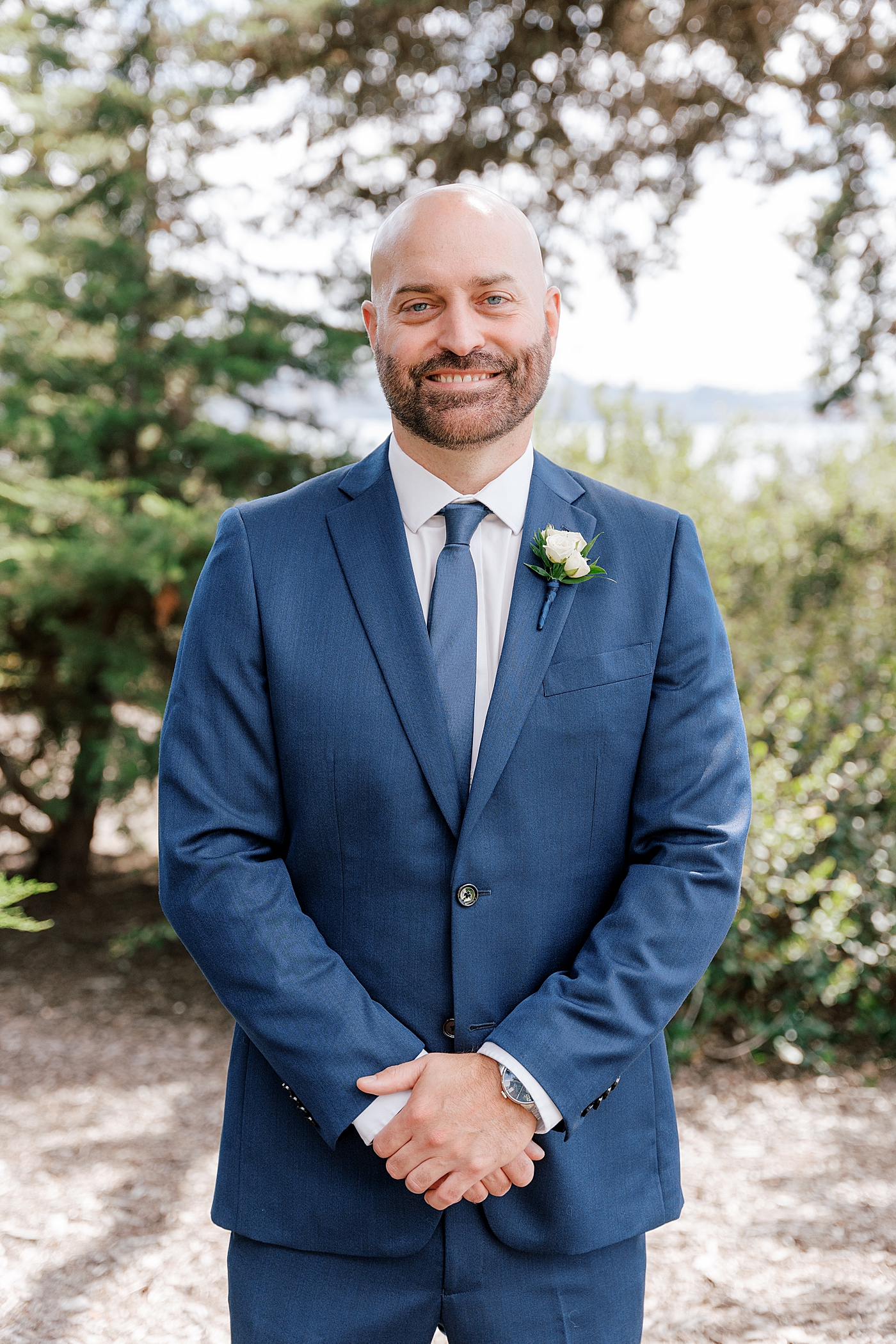 Groom in navy suit smiling at the camera with hands crossed in front | Image by Hope Helmuth Photography