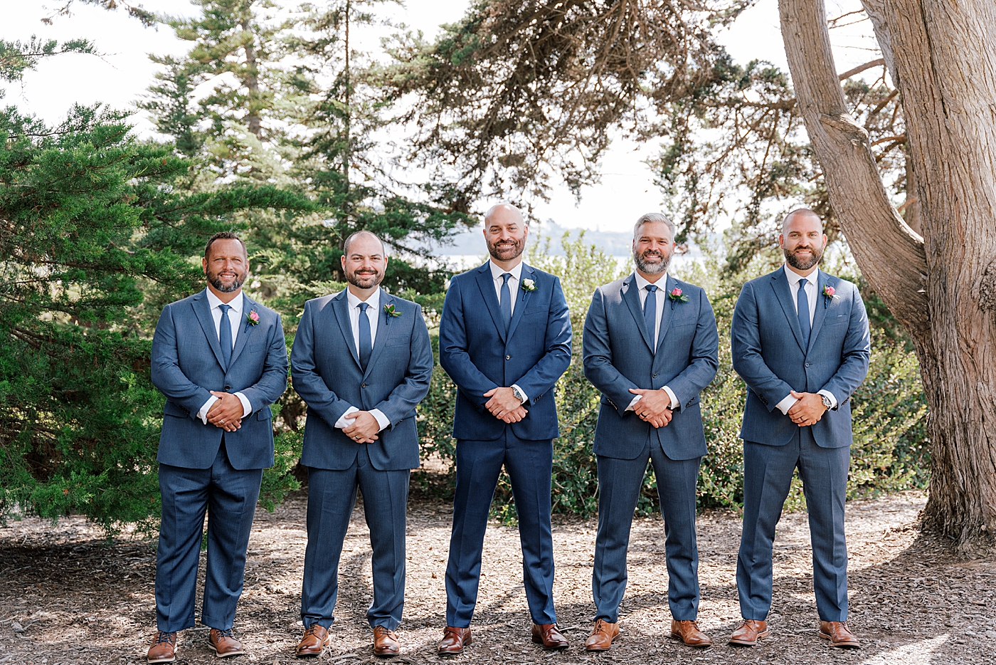 Groom and groomsmen in navy suits lined up side by side smiling at the camera | Image by Hope Helmuth Photography