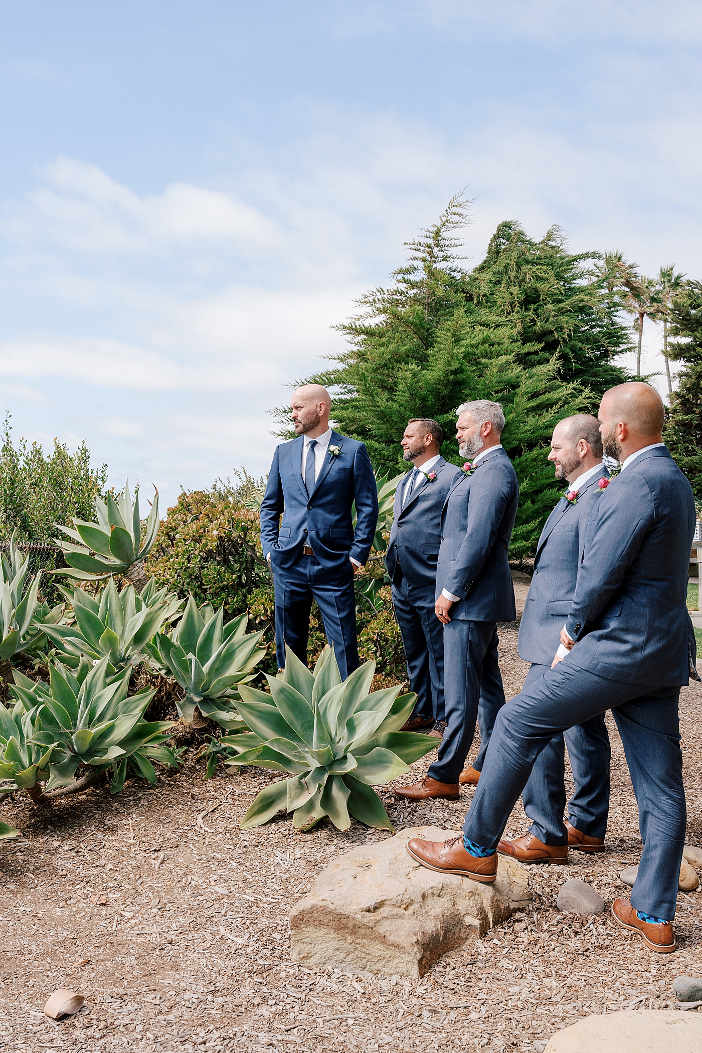 Groom and groomsmen in navy suits posed in nature looking out at the ocean | Image by Hope Helmuth Photography