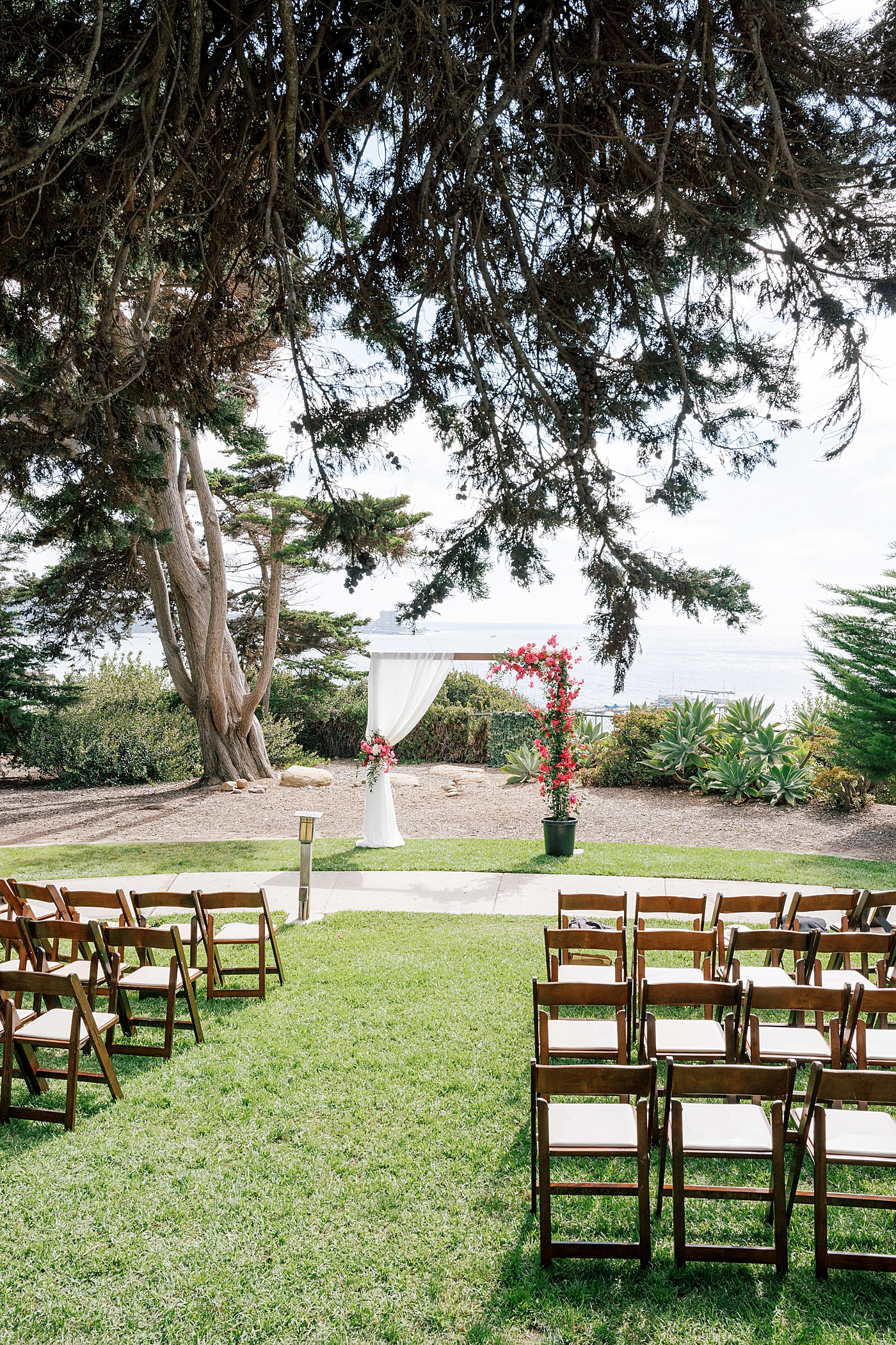 Image of a tropical wedding ceremony site with folding chairs and squared-off arch covered in bright pink flowers | Image by San Diego Wedding Photographer Hope Helmuth
