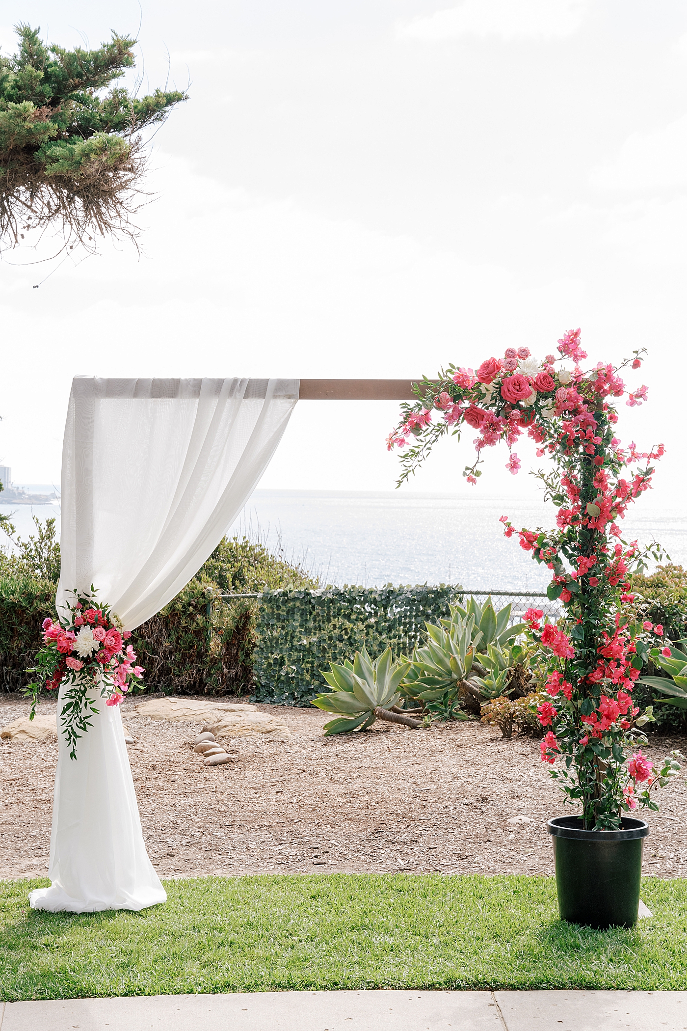 Closeup image of a tropical wedding ceremony site's squared-off arch covered in bright pink flowers | Image by Hope Helmuth Photography